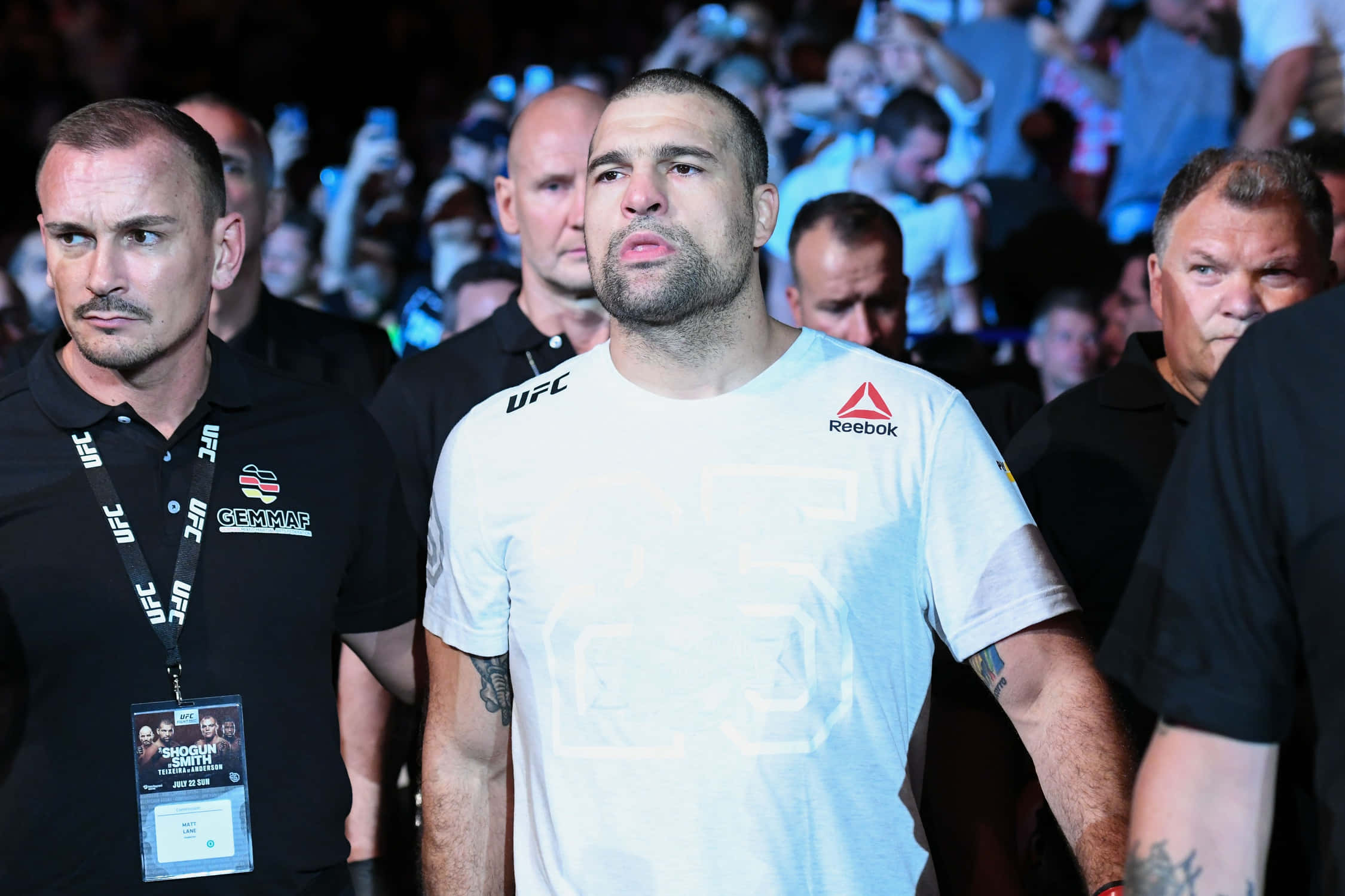馬烏里西奧·魯亞 UFC 競技之夜 壁紙 — 一位專注的綜合格鬥選手在明亮的場館燈光下，在UFC賽事中穿過粉絲和保安的人群。