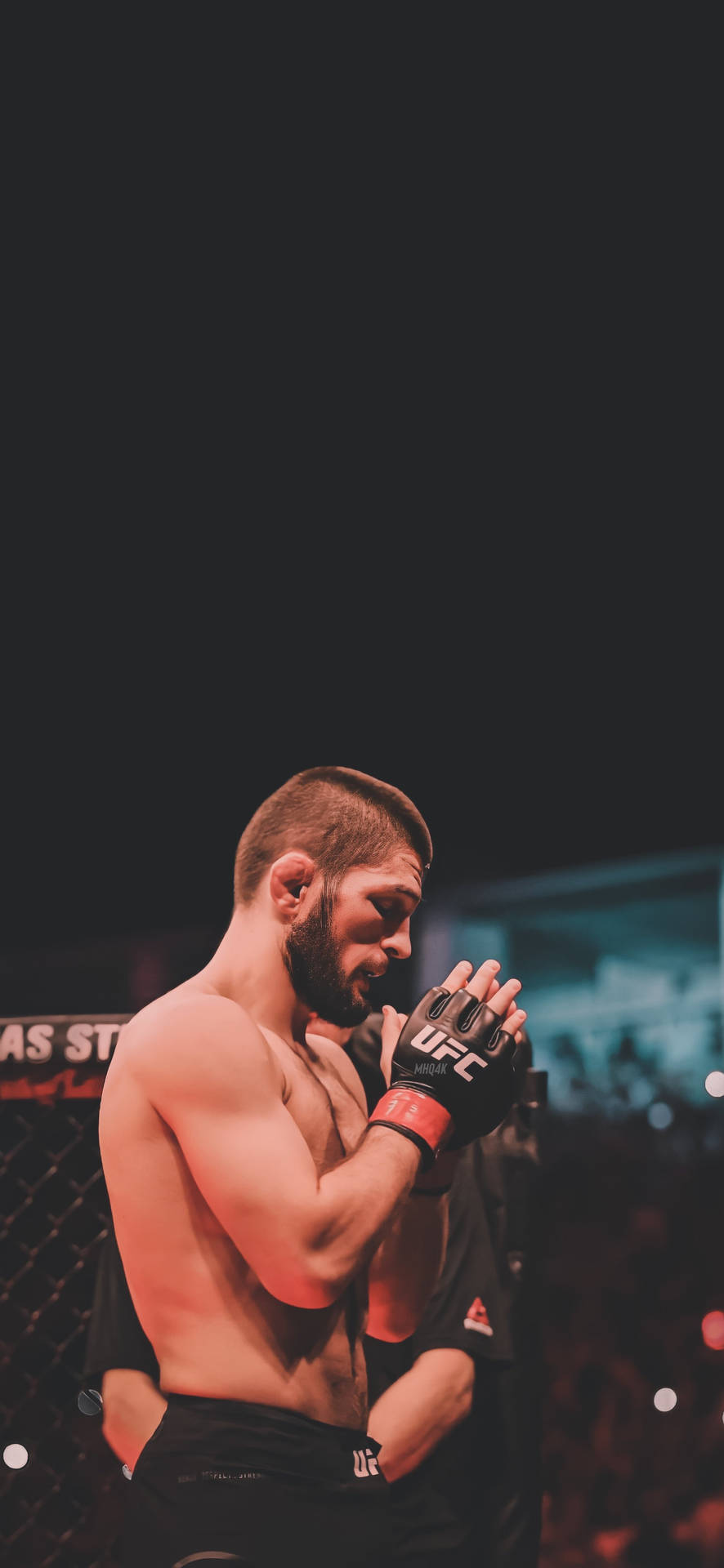 一位專注的MMA拳手穿著UFC裝備，雙手合十靠近臉部，站在八角籠內。