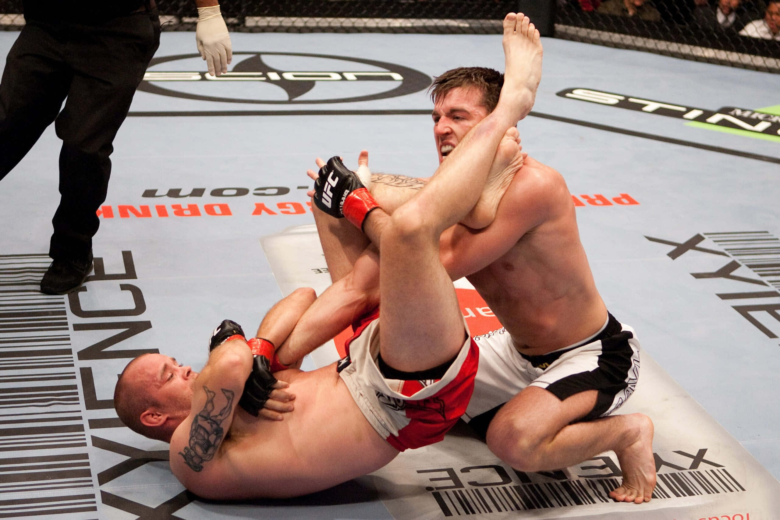 傑瑞米·霍恩參與UFC比賽 壁紙 — 兩名MMA拳手在品牌八角形墊上激烈纏鬥，裁判在旁緊密注視。
