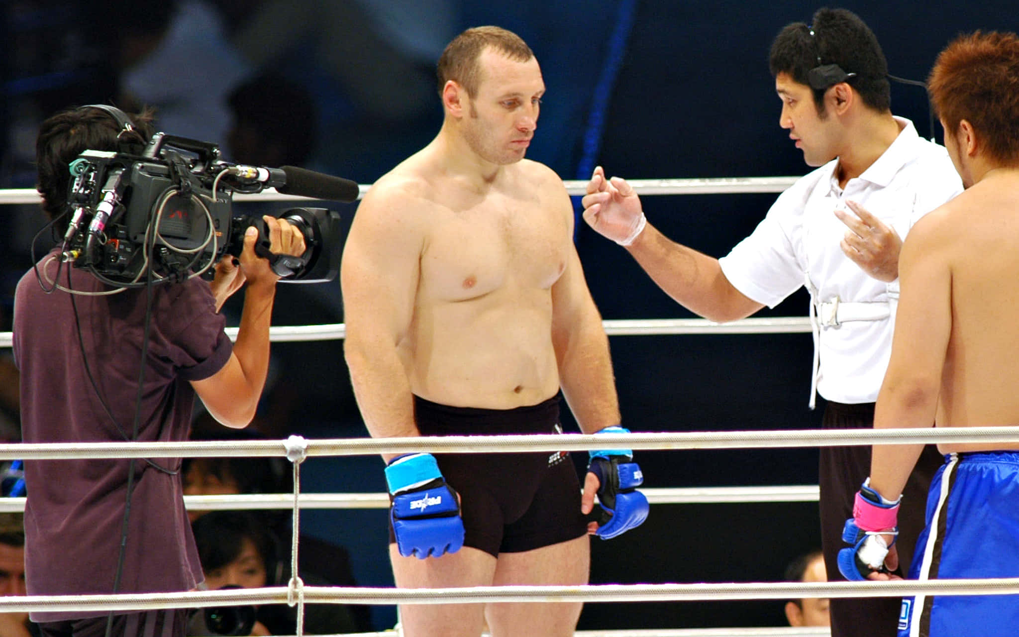 UFC MMA選手伊戈爾·沃夫恰寧 壁紙 — 兩名赤膊的拳手穿著黑色和藍色短褲站在拳擊台上，裁判做手勢，攝影師拍攝他們。