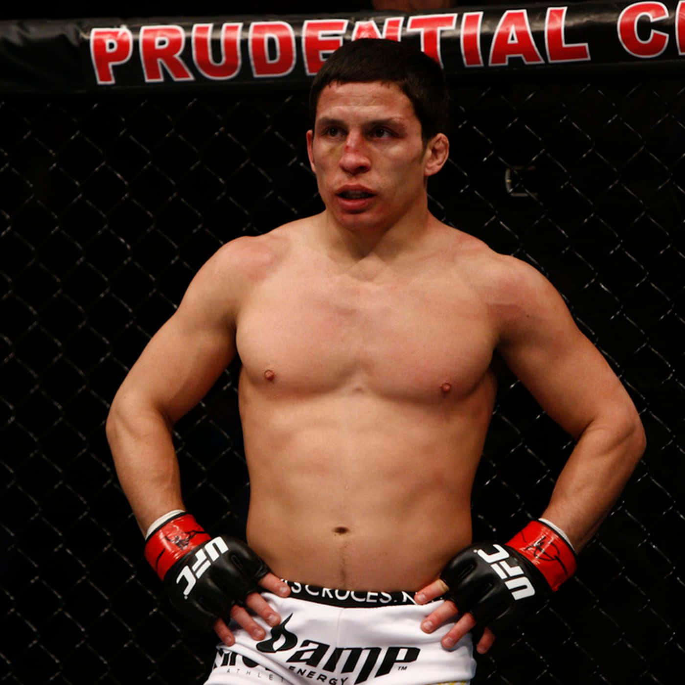 約瑟夫·貝納維德茲 UFC 資深格鬥士 壁紙 — 一名赤裸上身、滿臉鮮血的男性拳手，自信地站在UFC八角籠中，戴著紅黑手套。