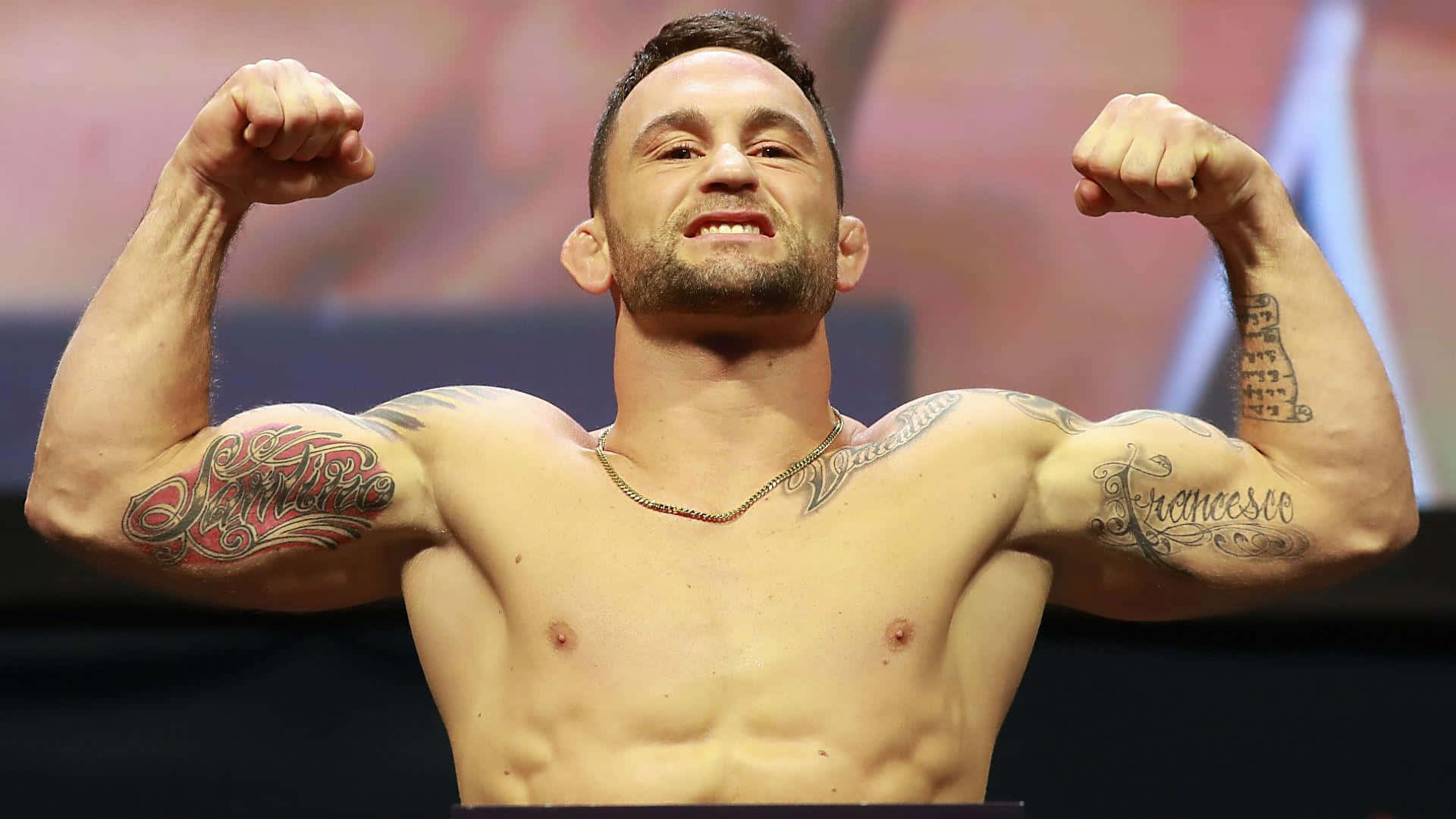 UFC 冠軍弗蘭基·愛德華賽場風采 壁紙 — 一個有紋身的肌肉男在明亮的舞台燈光下以勝利姿勢彎曲雙臂。