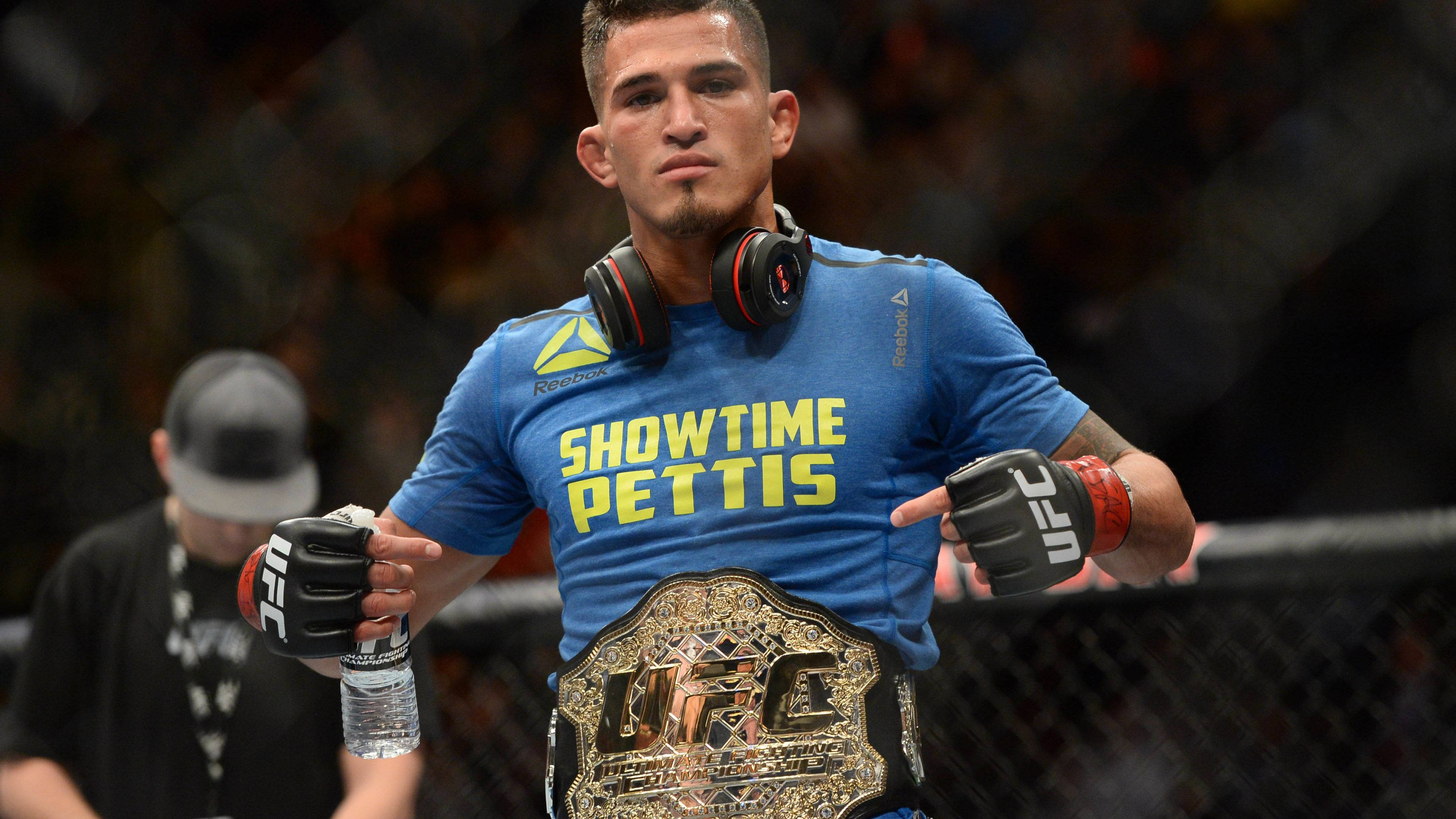 UFC 安東尼·秀時·佩蒂斯 壁紙 — 一位身穿藍色「Showtime Pettis」T恤的勝利UFC拳手，在八角籠內自豪地展示他的冠軍腰帶。