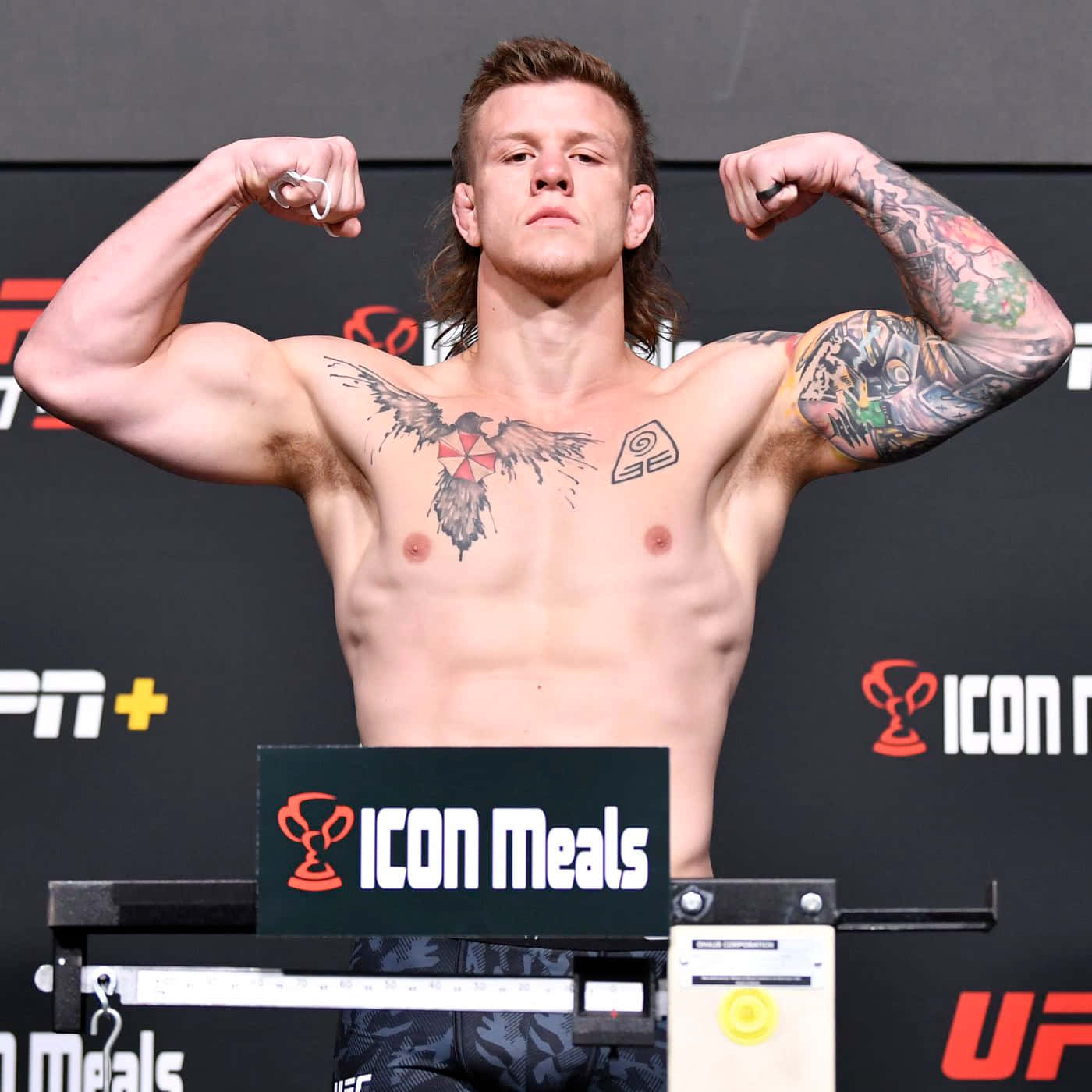 一位有紋身的 UFC 拳手在過磅活動中在磅秤上展示肌肉。