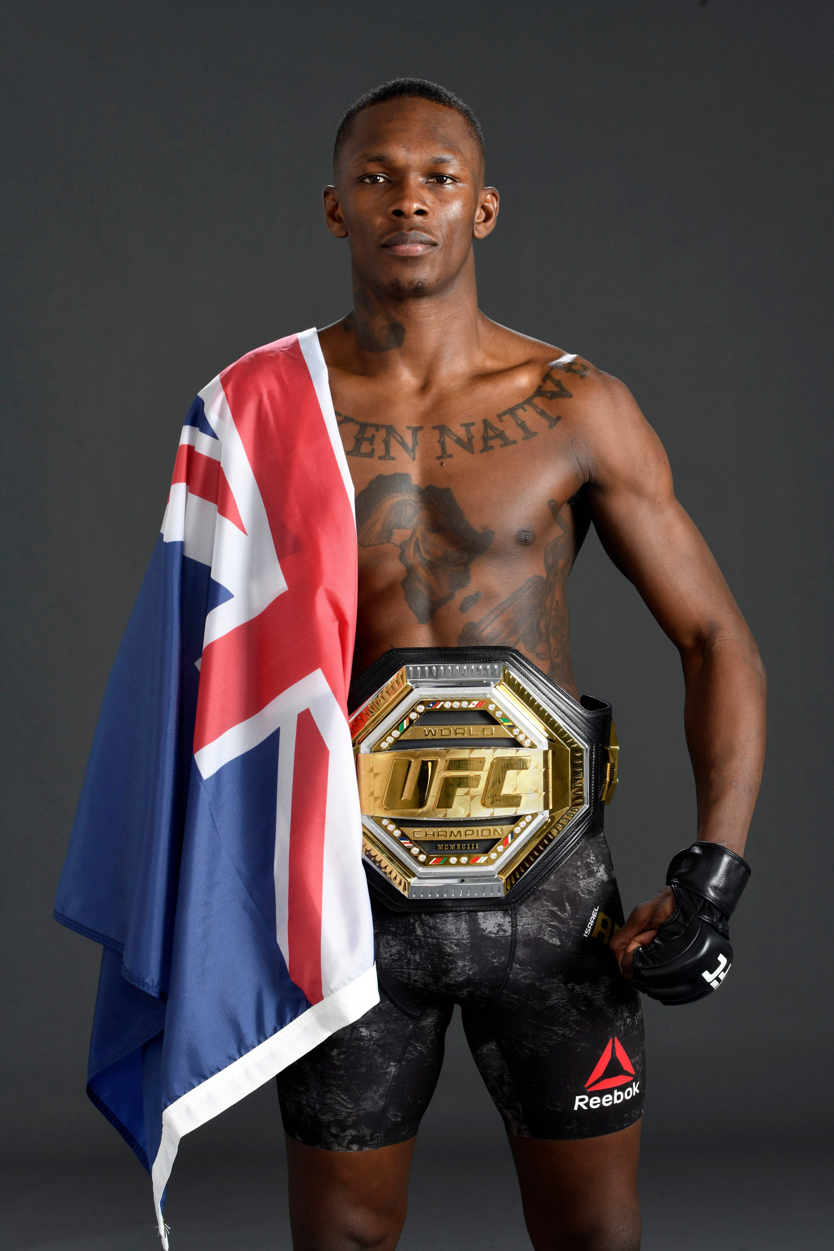 UFC冠軍以色列阿德esan亞肖像 壁紙 — 一位肌肉發達的UFC拳手自信地站著，腰間繫著冠軍腰帶，披著英國國旗，背景是黑暗的攝影棚。