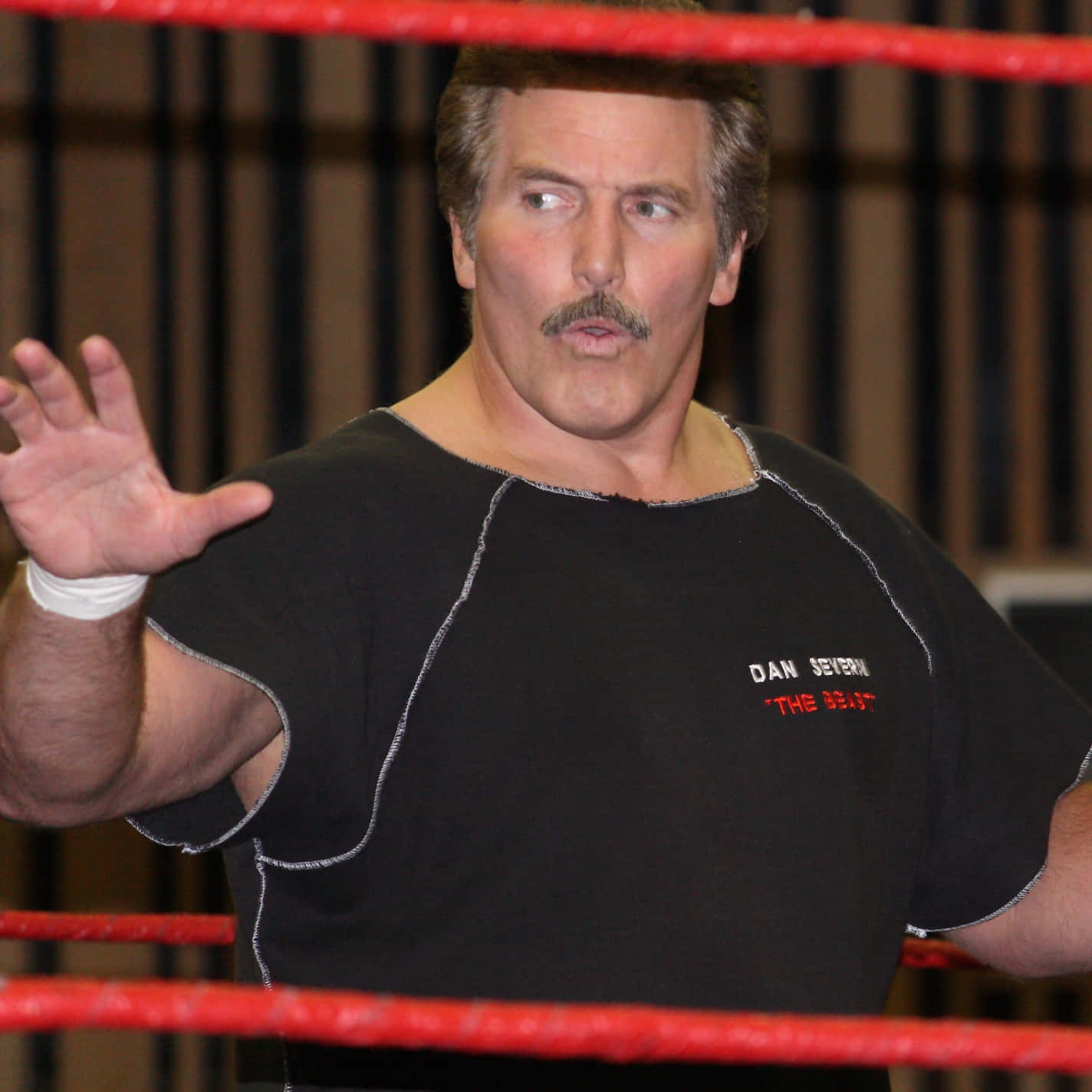 摔角手 Dan Severn 在擂台上穿著黑色襯衫，紅色繩索清晰可見。