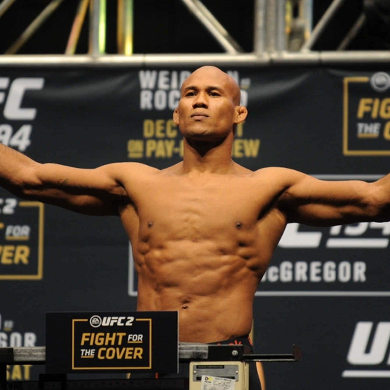 UFC封面戰賽事稱重 - 羅納爾多·蘇扎 壁紙 — 一位肌肉發達的UFC拳手在明亮的場館燈光下，自信地張開雙臂站在體重磅上進行稱重活動。