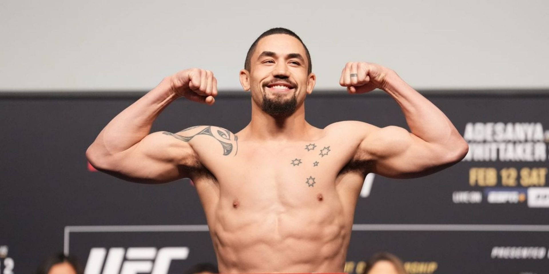 UFC明星羅伯特·惠特克展現戰鬥力量 壁紙 — 一位肌肉發達的UFC拳手在稱重活動中自信地微笑並彎曲手臂。