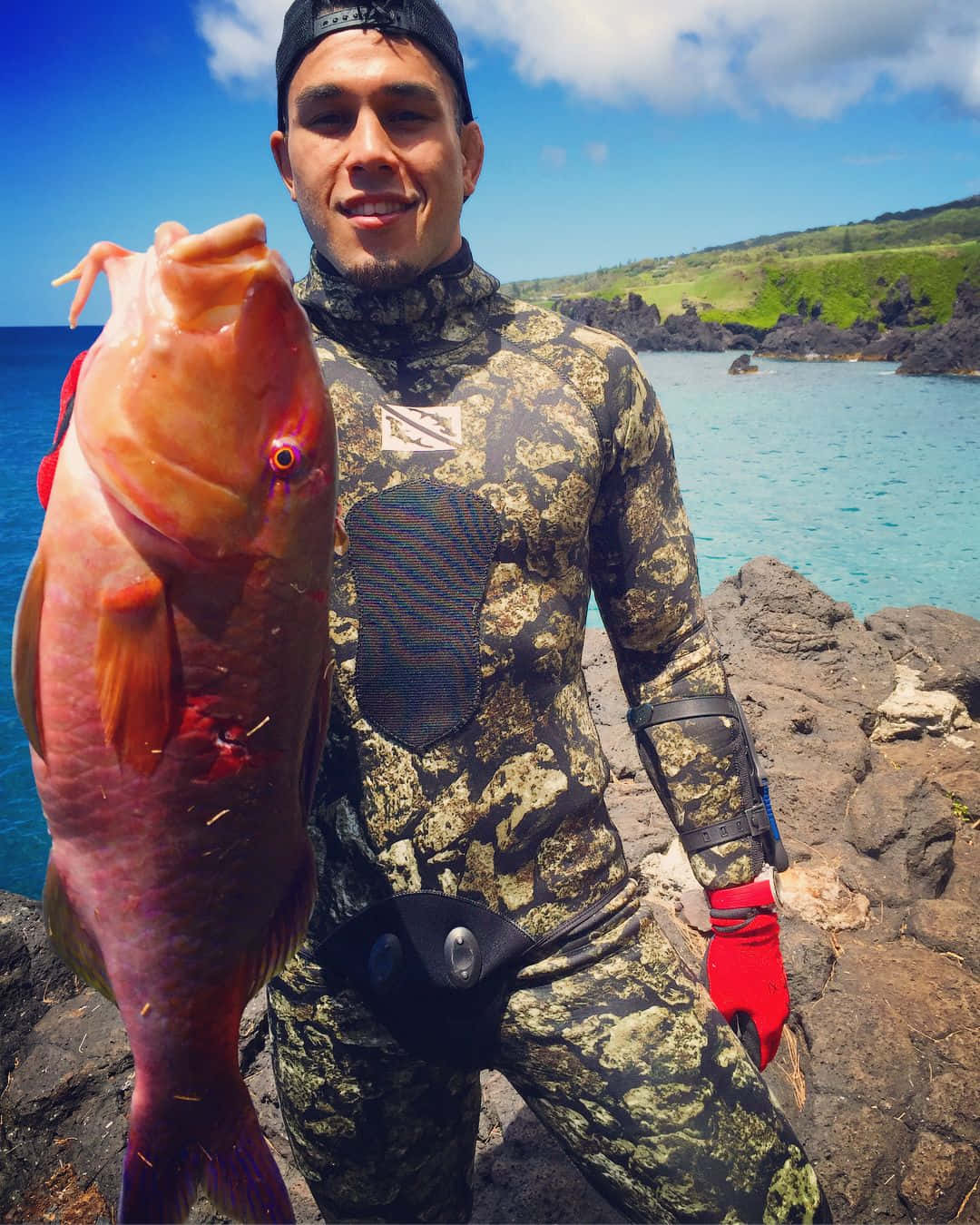 穿著潛水衣的男人在岩石海灘上拿著大粉紅魚
