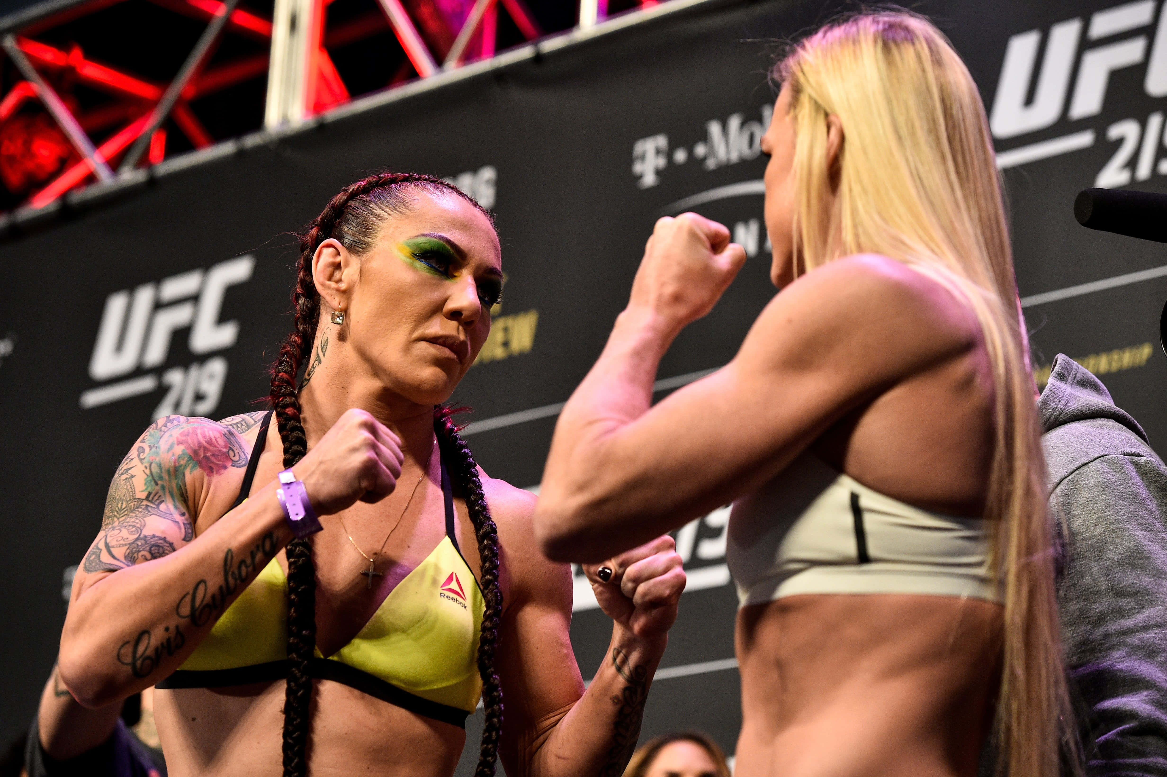 UFC選手Cris Cyborg與Holly Holm儀式稱重對峙照 壁紙 — 兩名女性UFC拳手在明亮的場館燈光下進行緊張的賽前對峙。