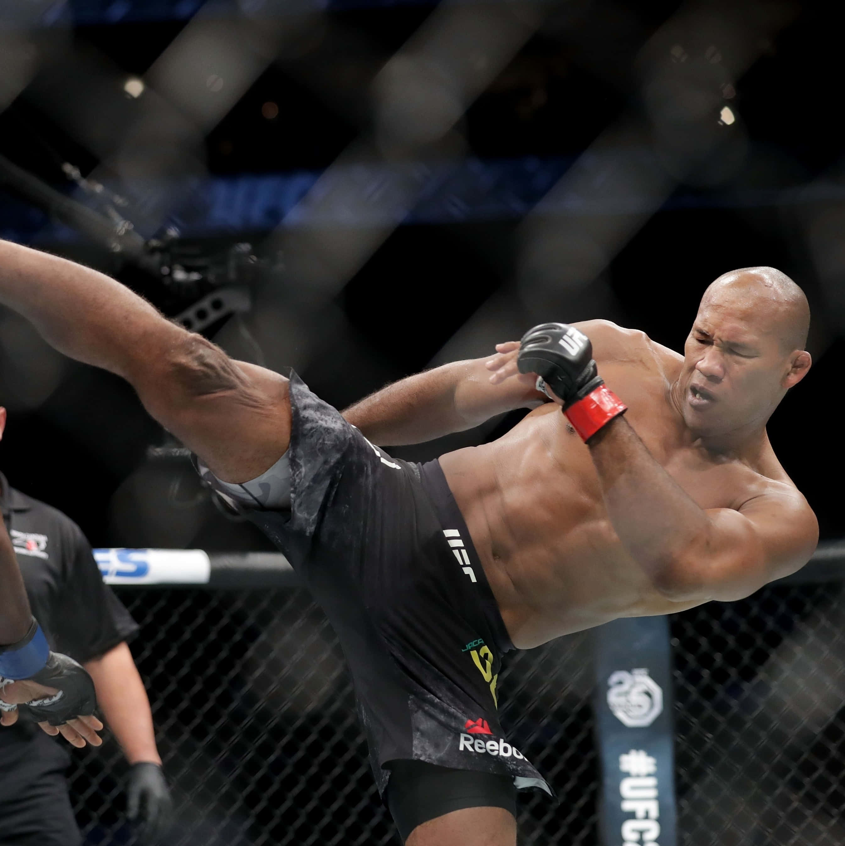 UFC選手羅納爾多·蘇薩施展高踢腿 壁紙 — 一名肌肉發達的拳手在明亮的場館燈光下，於UFC八角籠內執行高踢。