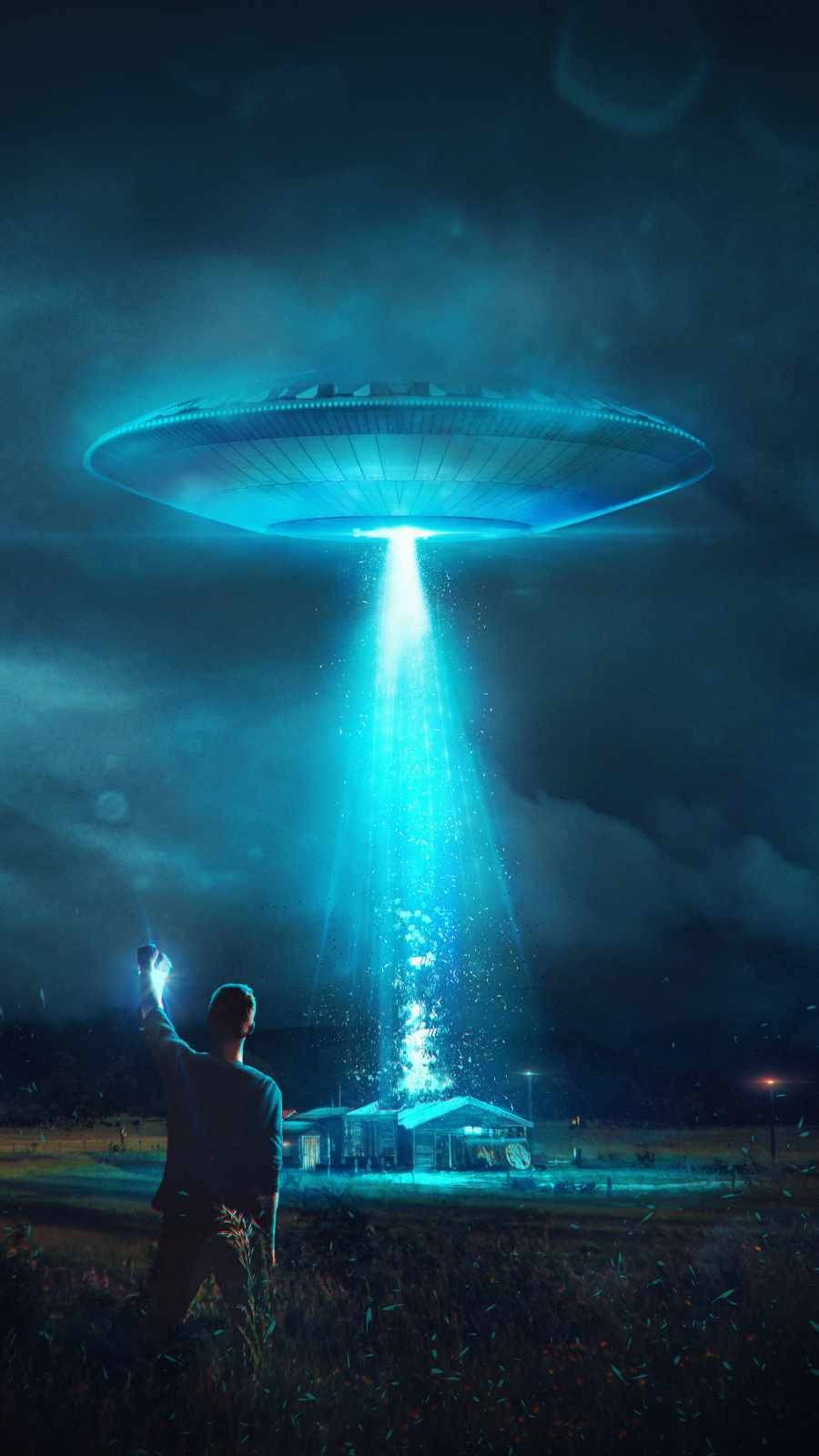 夜晚田野中的人舉起手電筒照向房子上方發光的不明飛行物。