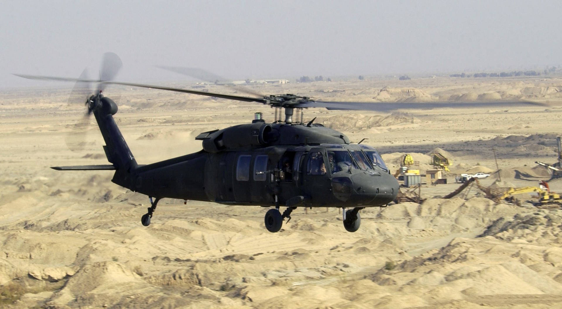 黑色軍用直升機低空飛越沙漠建築工地。