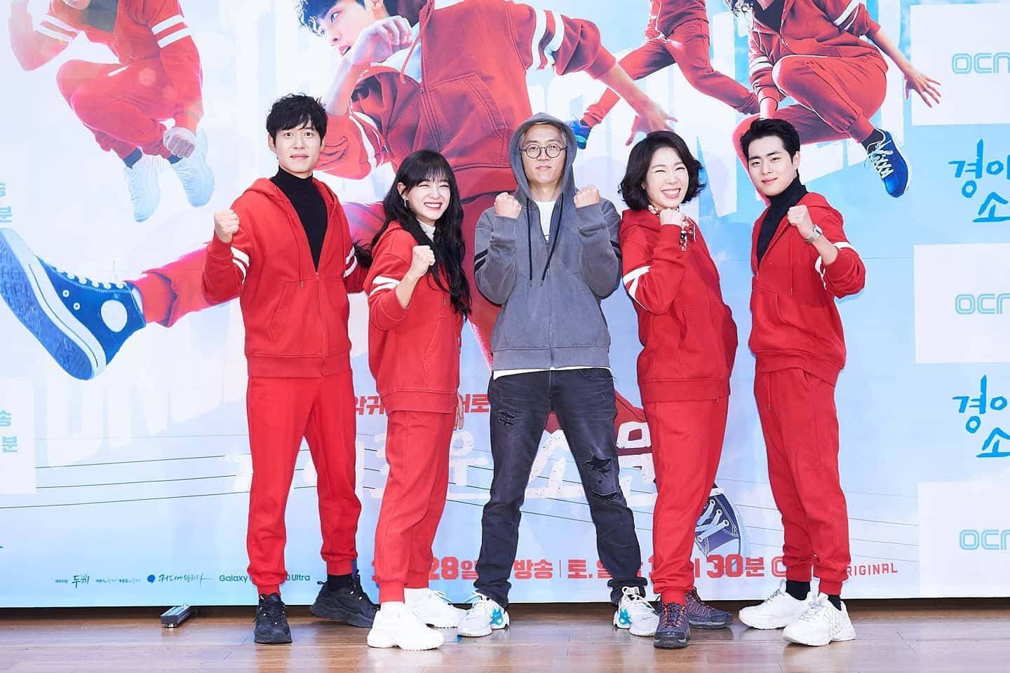 五個微笑的人身穿紅色運動服在宣傳活動中擺姿勢。