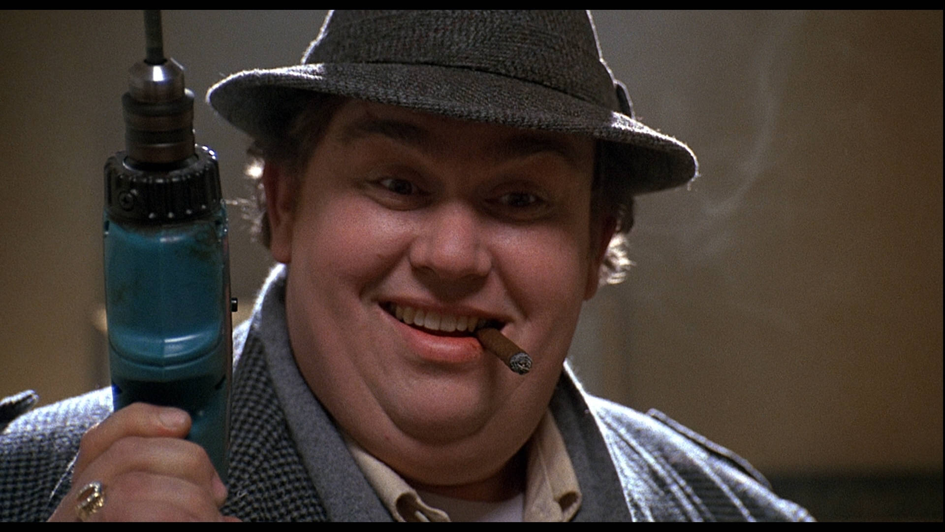 《Uncle Buck》場景約翰·坎迪 壁紙 — 一個戴著費多拉帽、穿著千鳥格大衣的男人咧嘴笑著，一手拿著藍色電鑽，一手抽著雪茄。