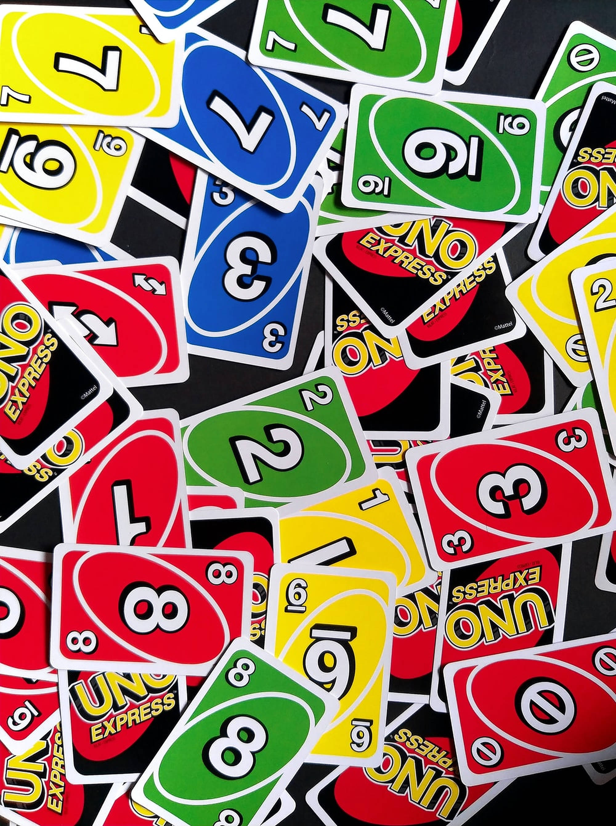 Uno 家庭卡牌遊戲 壁紙 — 一堆色彩繽紛、混亂的Uno Express卡牌，有紅色、黃色、綠色和藍色，數字和符號重疊在一起。