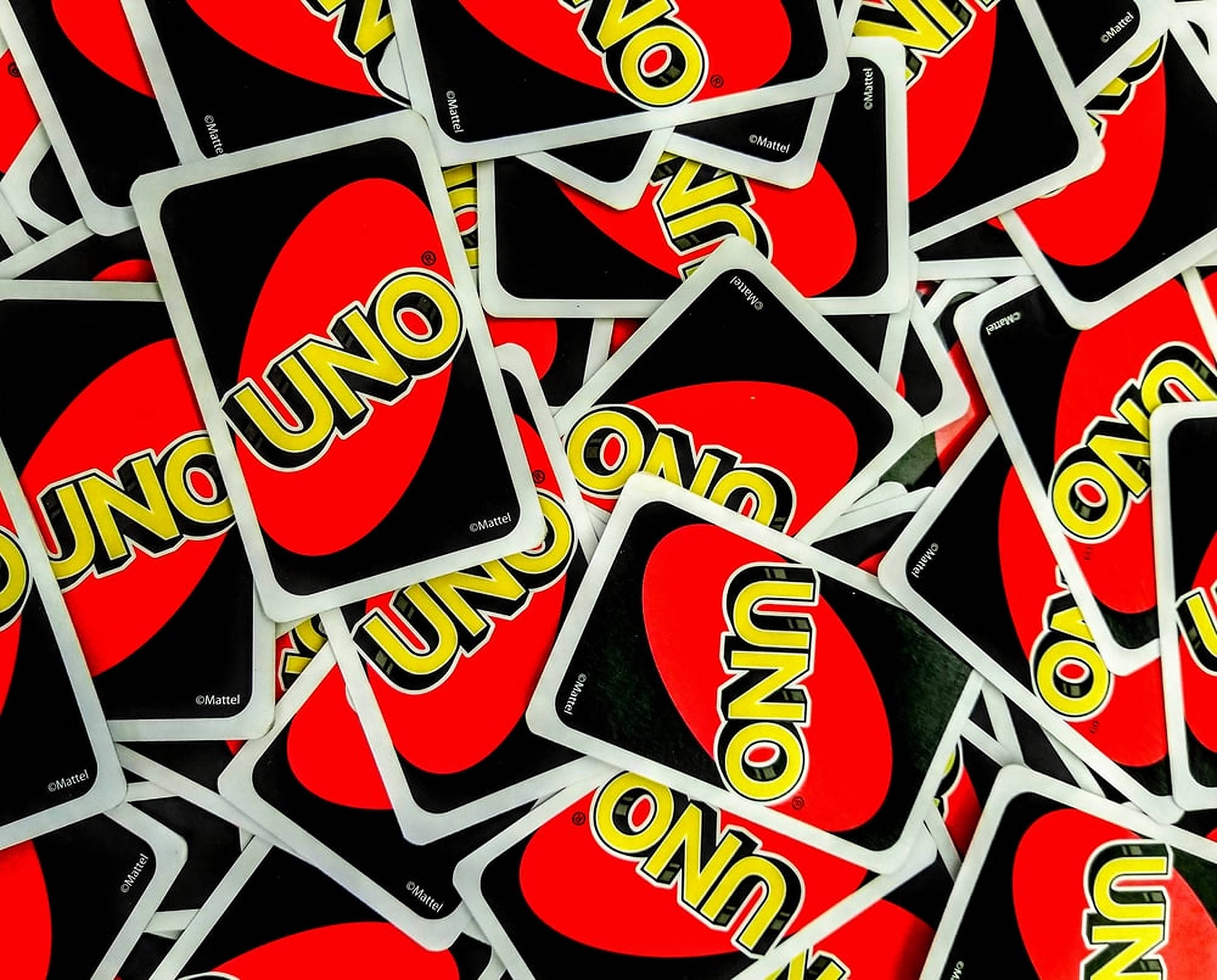 Uno撲克牌 壁紙 — 一堆鮮豔的紅色、黑色和黃色UNO卡牌，以混亂而有趣的圖案散落。