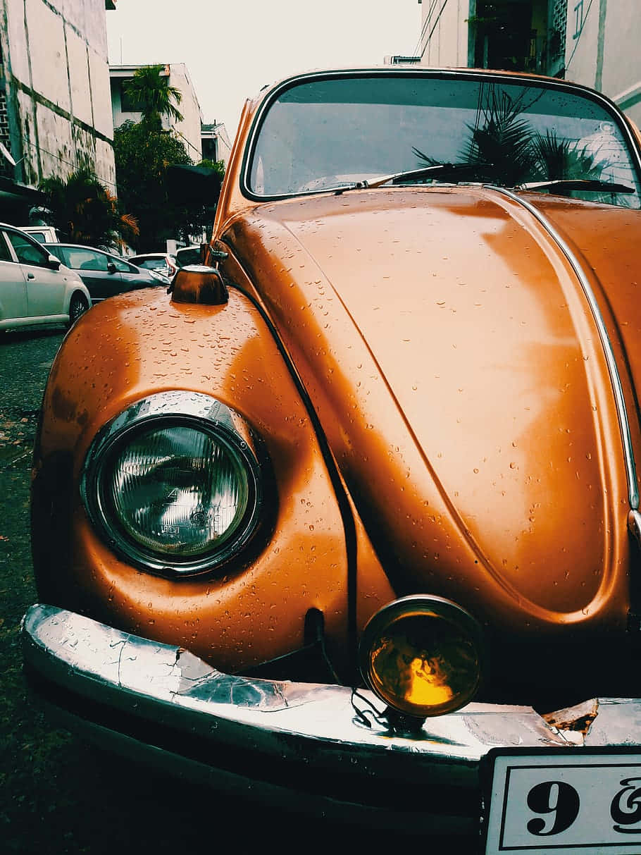 現代福斯Up! 城市生活好夥伴 壁紙 — 一輛復古橙色福士甲蟲車在陰天下的城市小巷中閃爍著雨滴。
