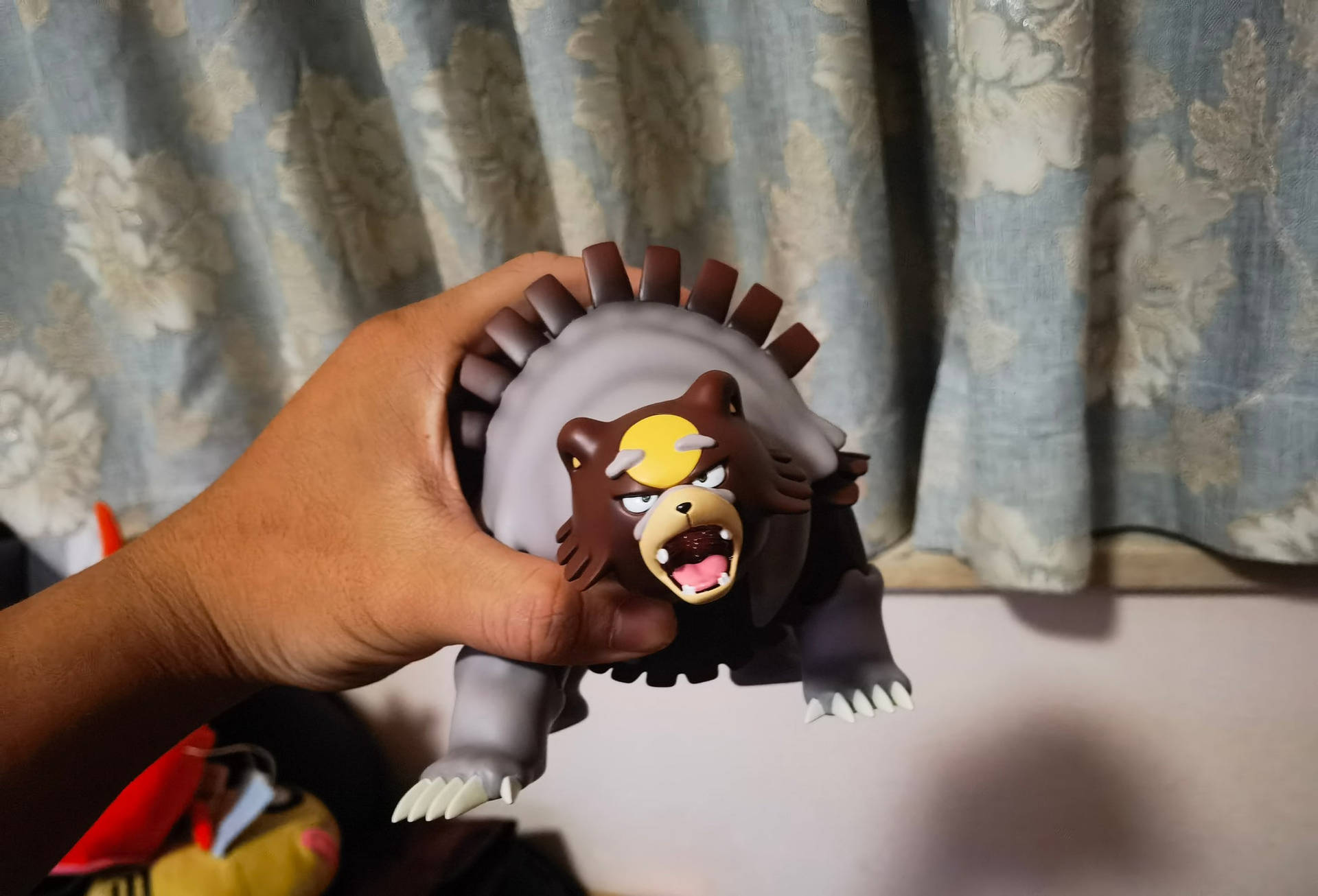 手拿著背部有尖刺、表情憤怒的Ursaring Pokémon玩具。