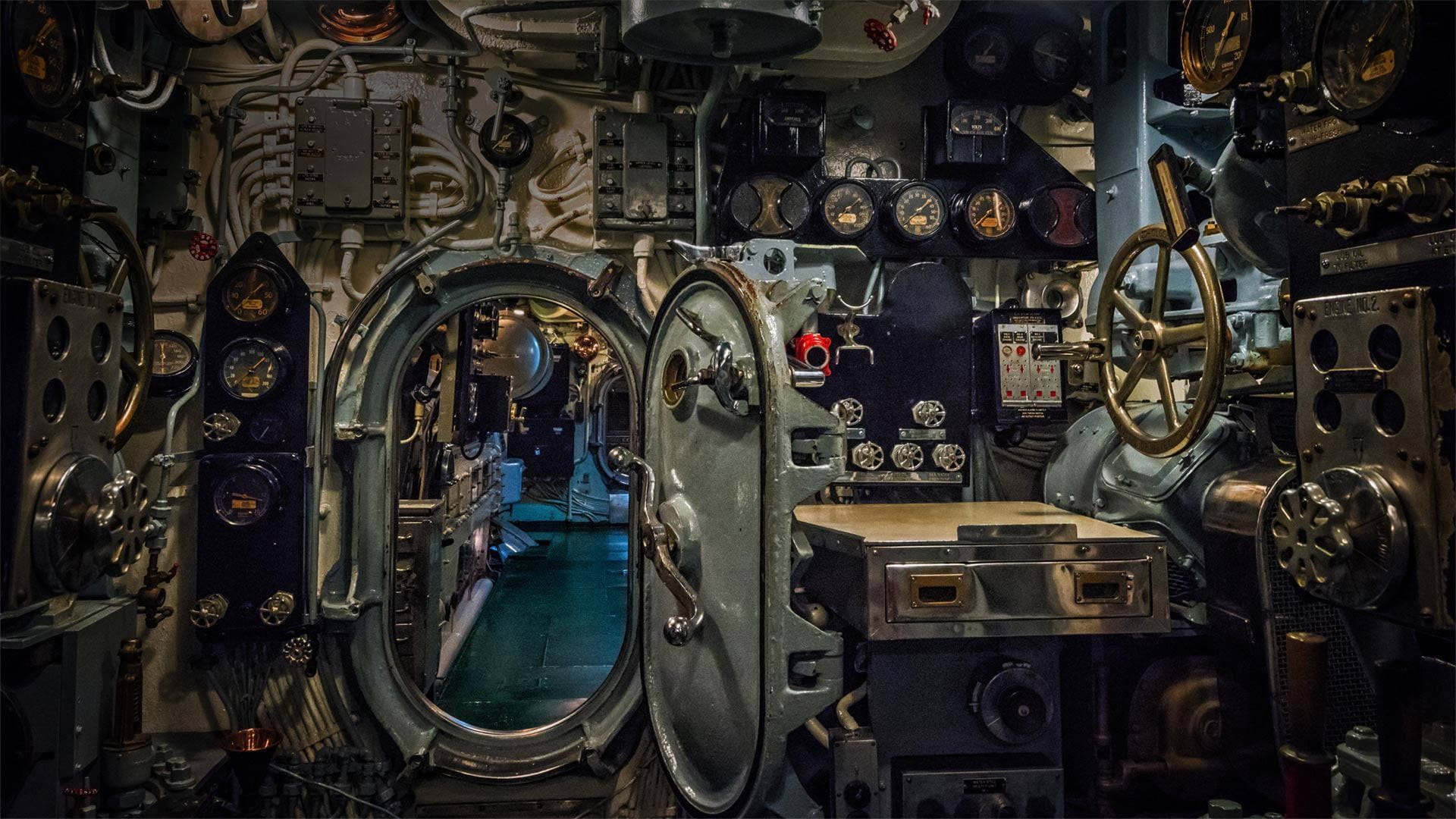 USS 阿拉巴馬號戰艦內部潛艇 壁紙 — 燈光昏暗的潛艇控制室，充滿了復古儀表、槓桿，以及一個打開的大型艙口，露出青綠色的走廊。