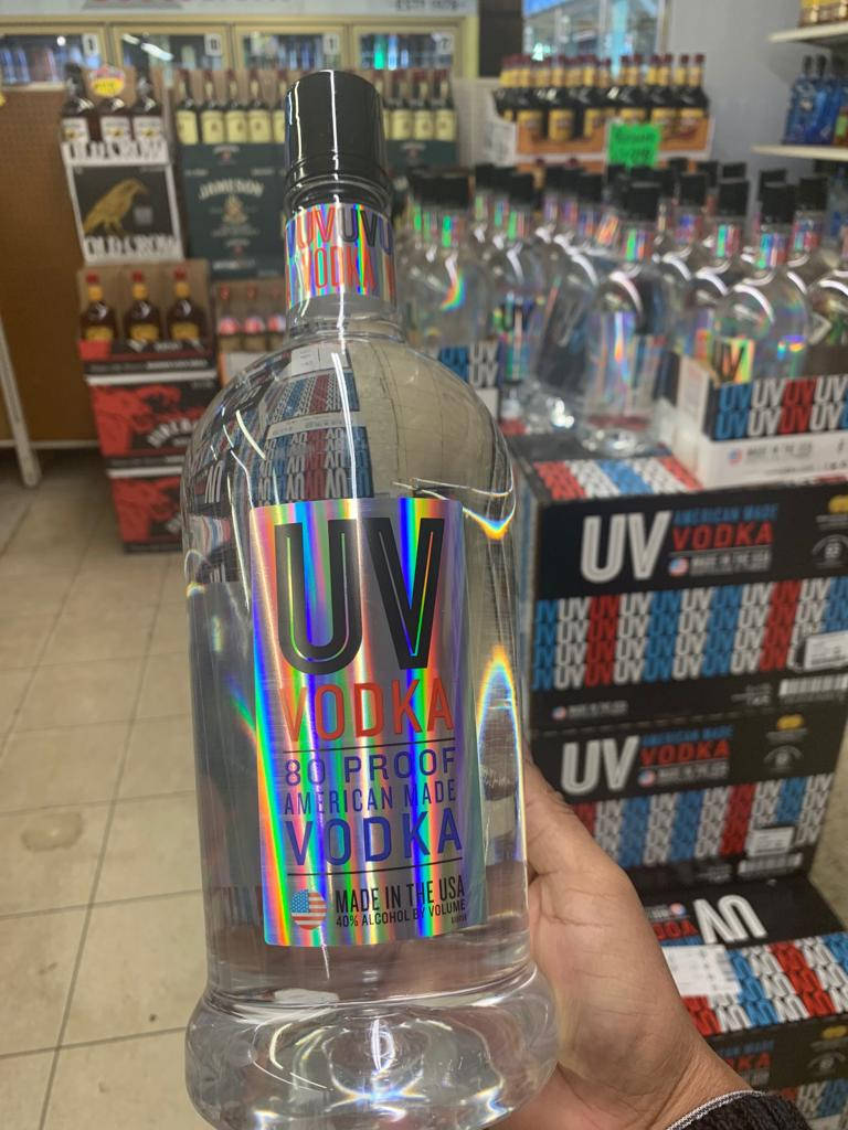 精緻 UV 伏特加銀版，展現優雅氣質 壁紙 — 一隻手在酒舖通道上拿著一個帶有彩虹全息標籤的大樽UV伏特加。