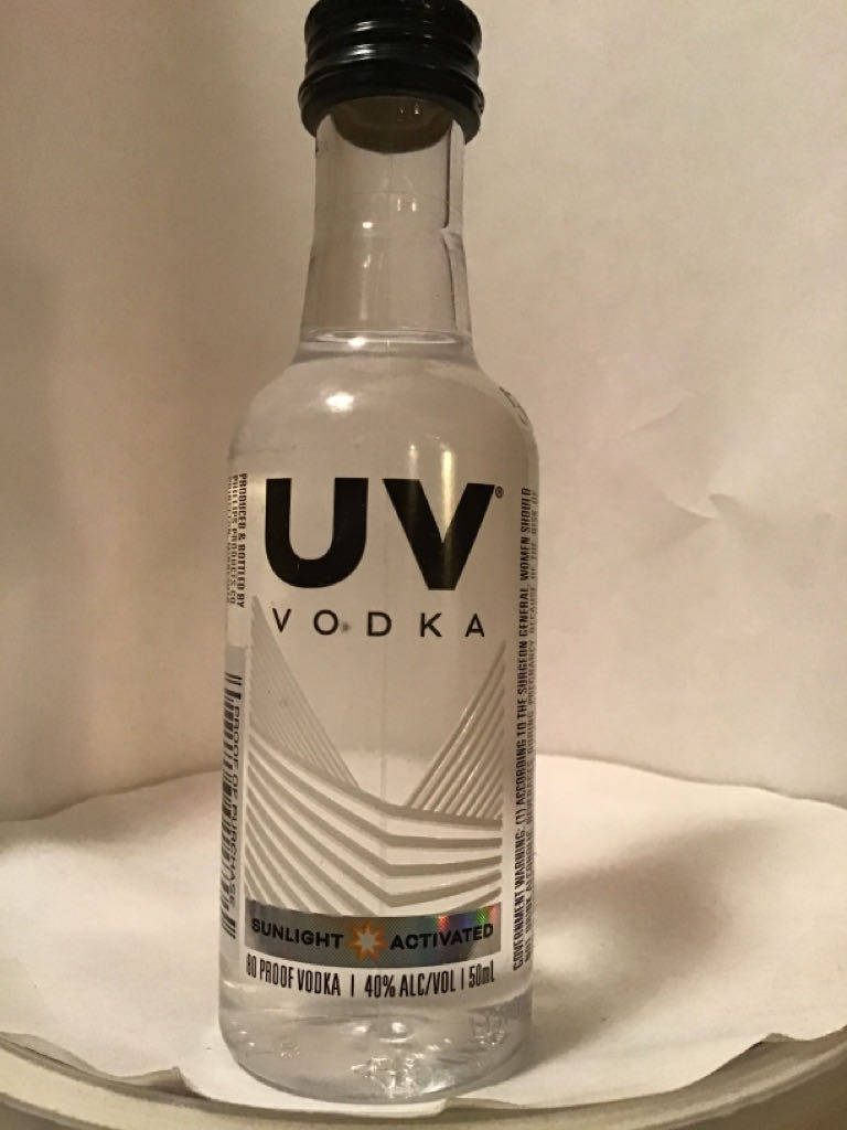 一個細細嘅透明伏特加酒樽，黑色樽蓋同幾何標籤，喺白色紙巾上面。
