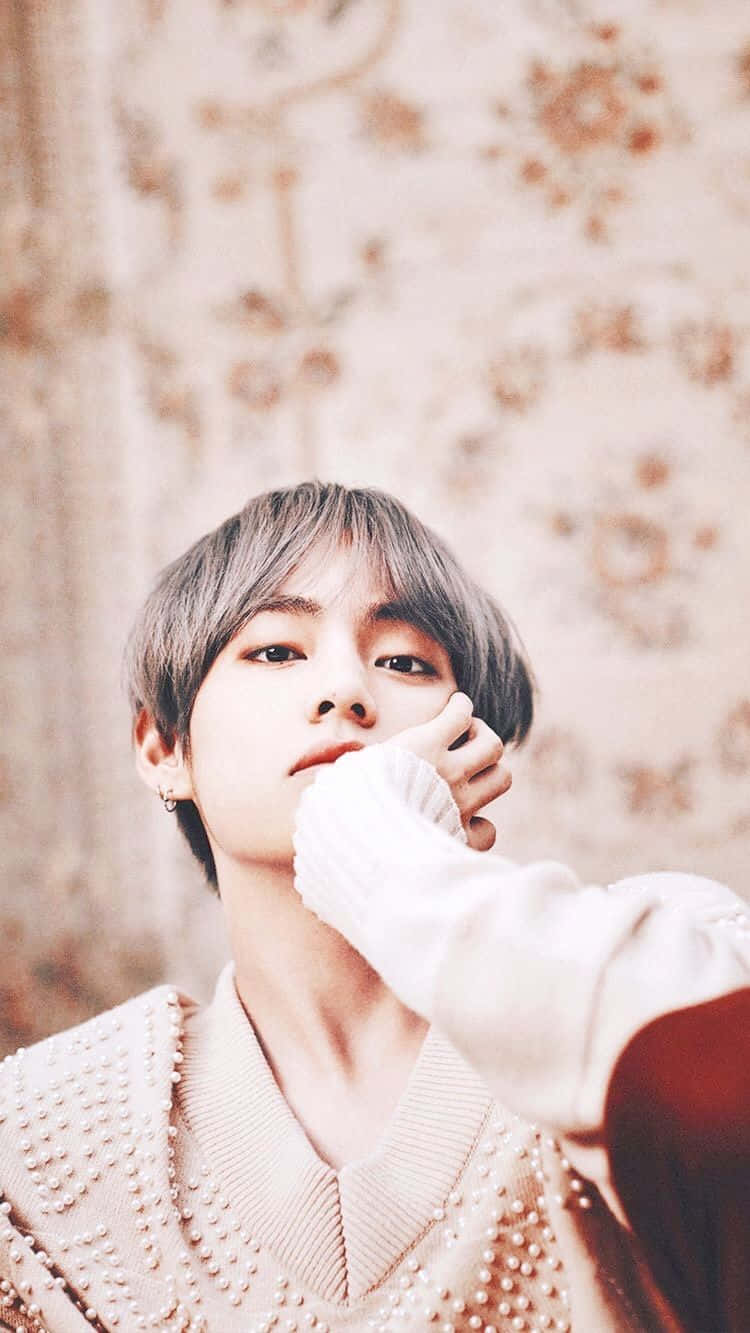 V BTS 手機中性風 壁紙 — 一位短灰髮、身穿白色毛衣的年輕男子，輕輕地將下巴貼在花卉壁紙背景上。