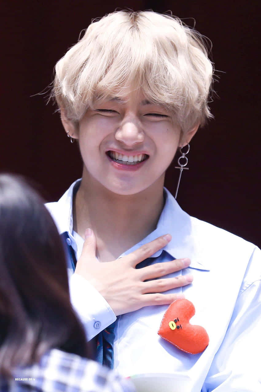 V BTS 手機版開心時刻 壁紙 — 一位金髮年輕男子穿著白襯衫和紅色心形別針，開懷大笑。
