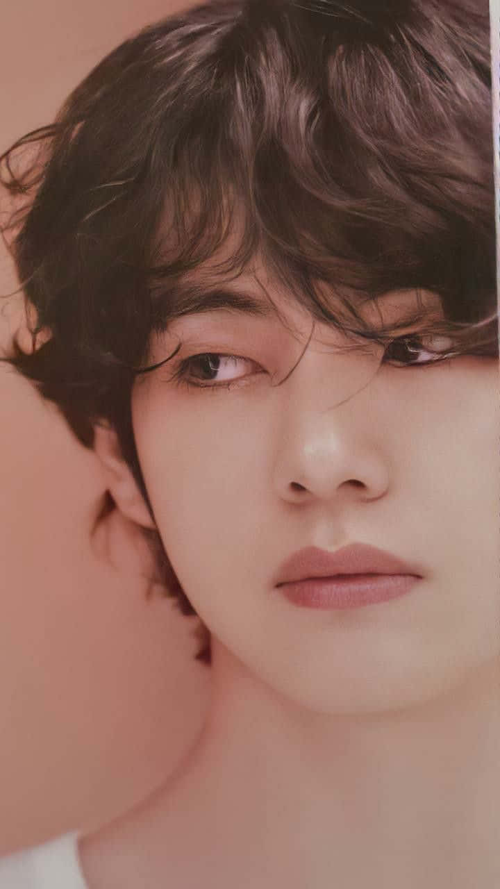 V BTS 手機美學風 壁紙 — 年輕深色波浪髮男士的頭像特寫，配以柔和粉紅背景。