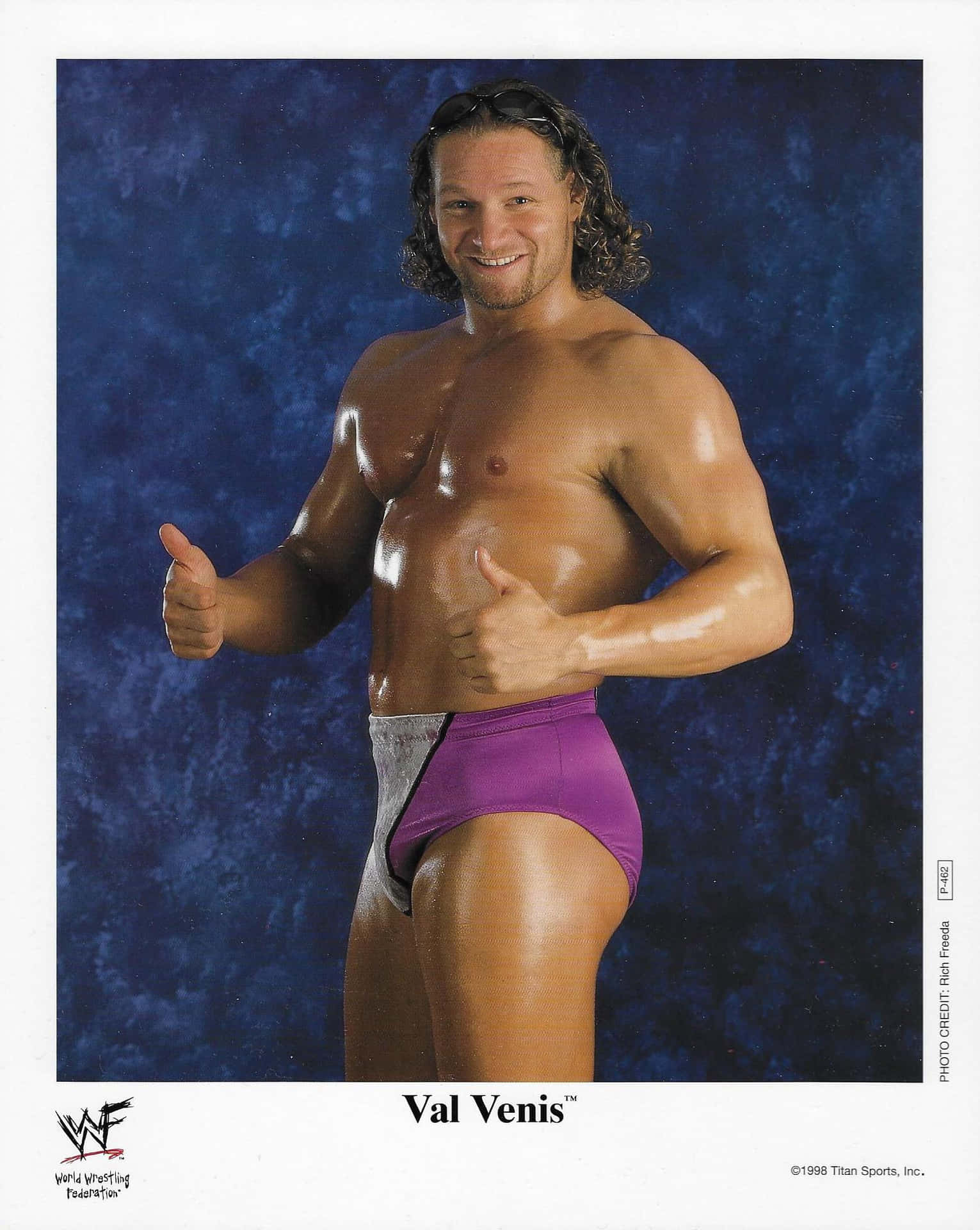 摔角手 Val Venis 穿著紫色短褲，在藍色背景前豎起雙拇指。