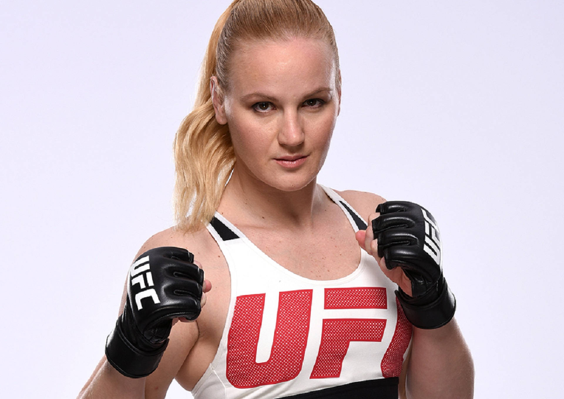 Valentina Shevchenko UFC 战鬥者肖像照 壁紙 — 一位專注的女性UFC拳手，身穿白色和紅色裝備，戴著黑色手套，在純白色背景前擺姿勢。