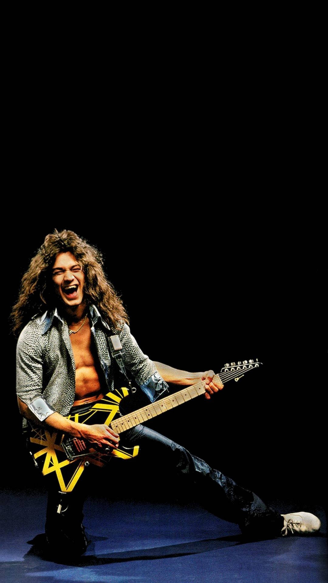 Van Halen 樂隊錄音室專輯 壁紙 — 一位長髮搖滾結他手在黑暗舞台上，於聚光燈下彈奏黃黑結他。
