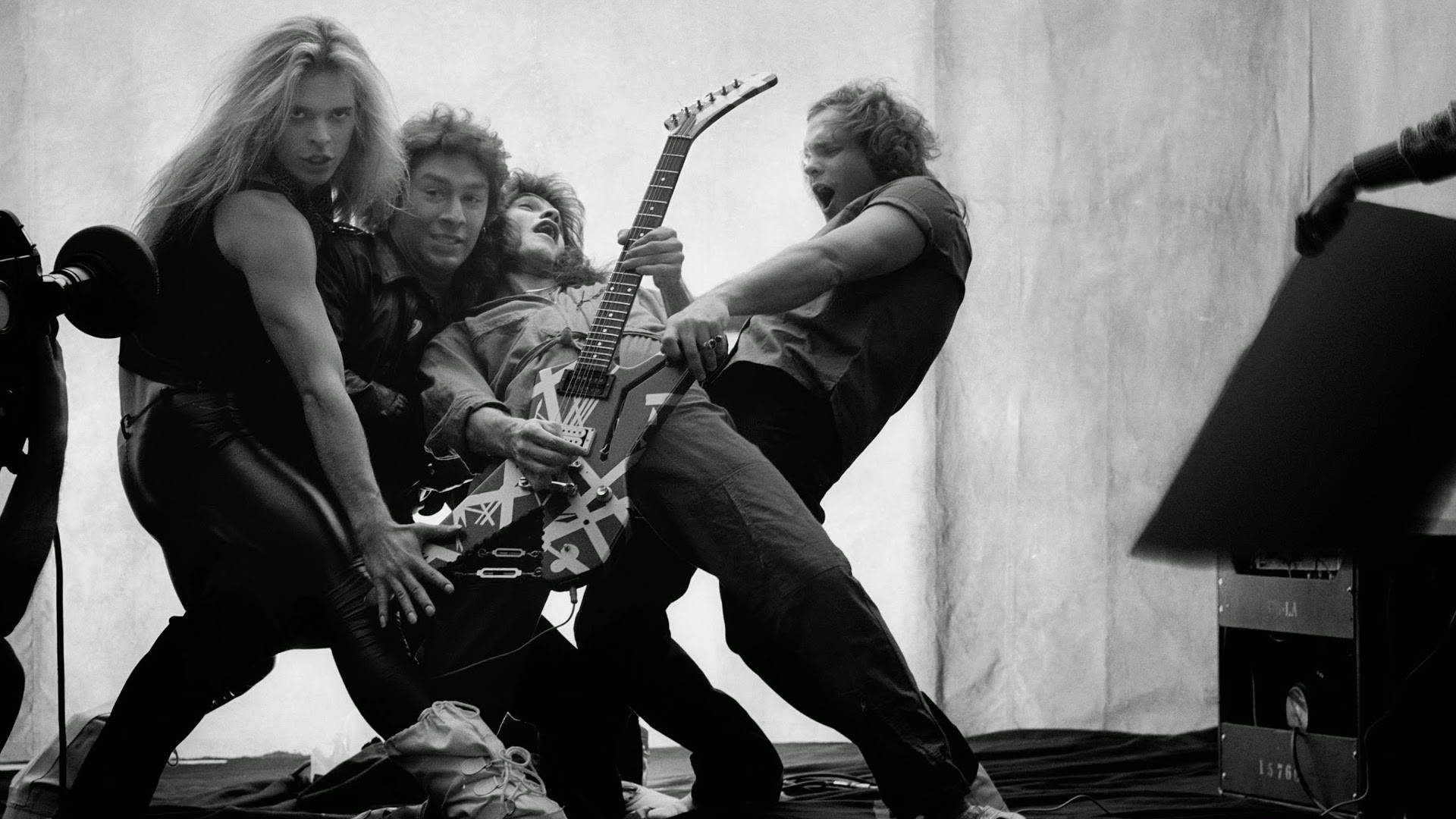 Van Halen 樂隊黑白影像 壁紙 — 一張黑白照片，金屬樂隊在舞台上充滿活力地表演，手持結他，表情強烈。