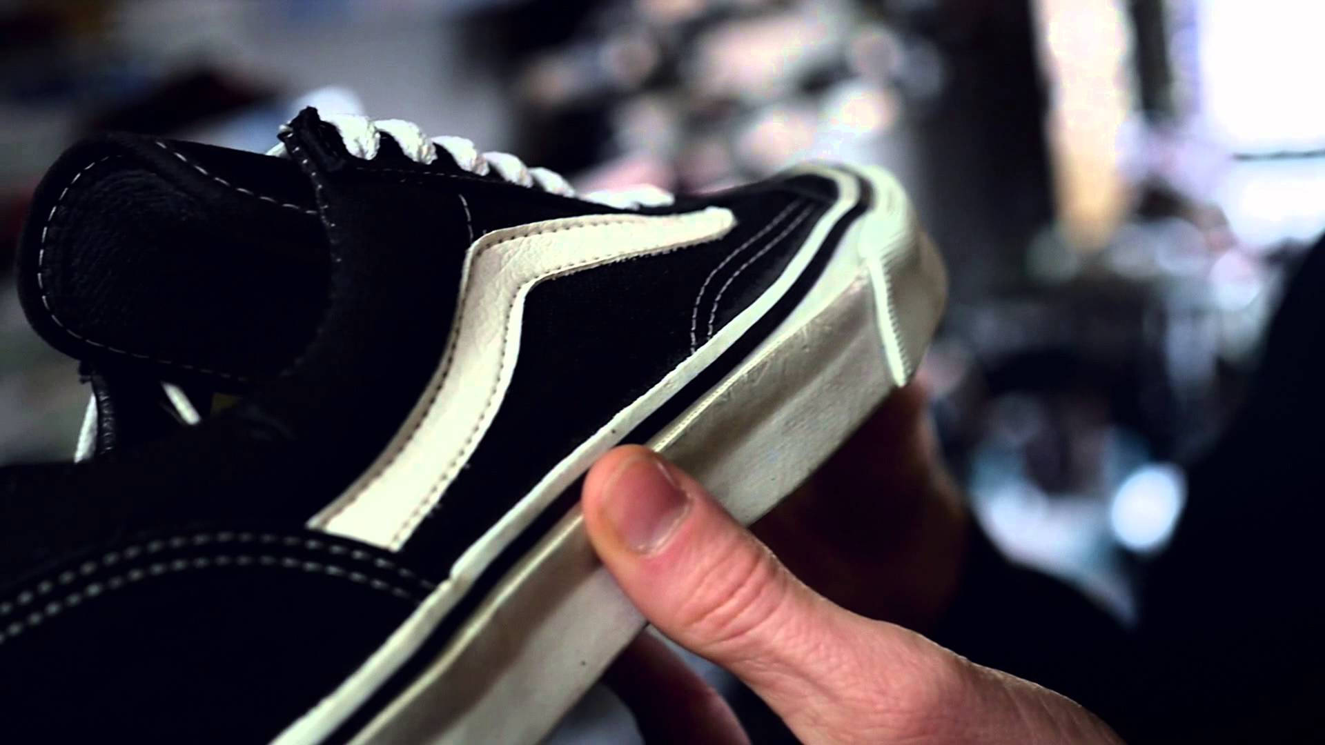 Vans Off The Wall 黑色鞋款 壁紙 — 一隻手拎住一對黑白Vans波鞋嘅特寫，可見縫線同磨損嘅鞋底。