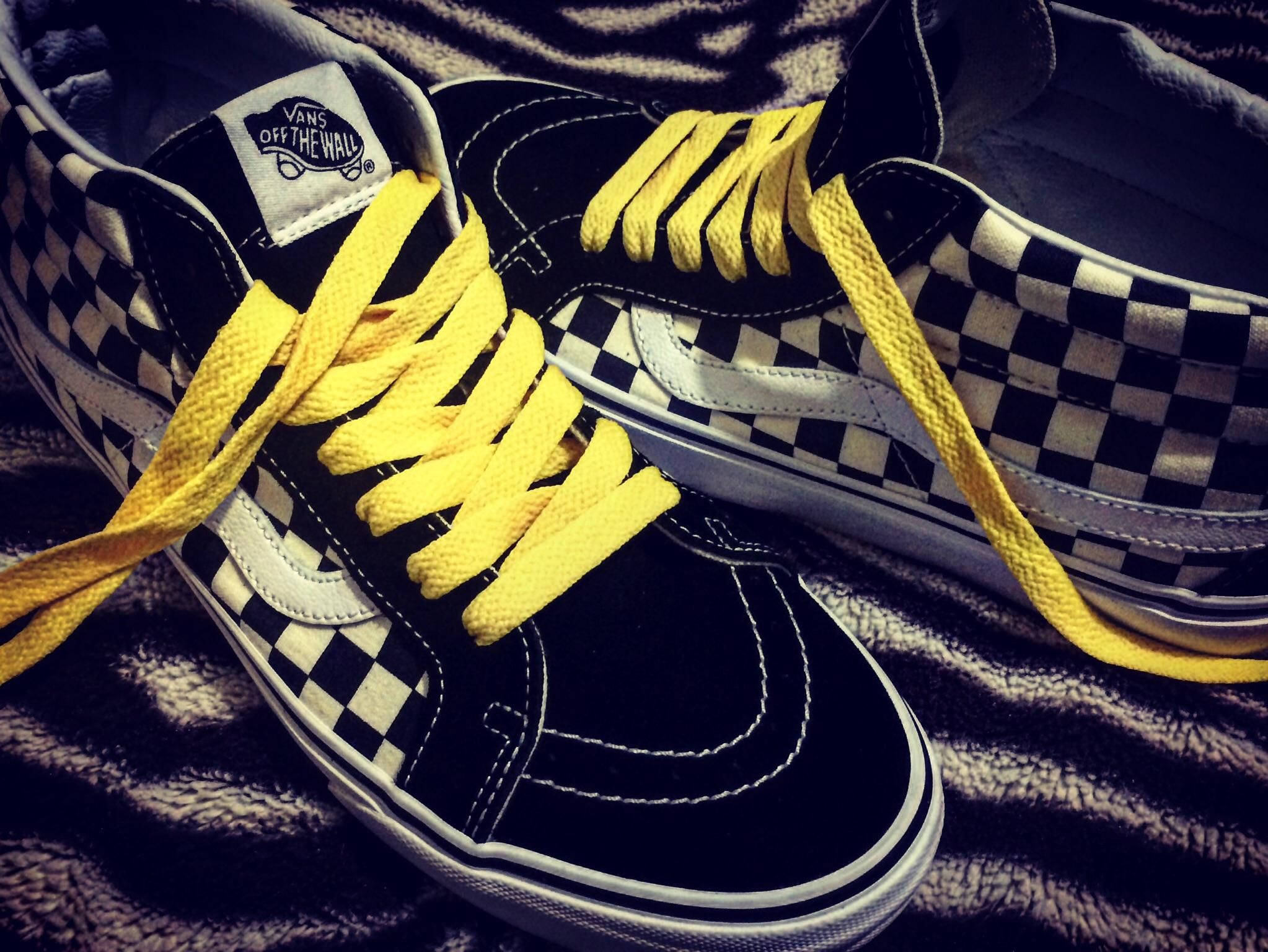 Vans Off The Wall 黃色鞋帶 壁紙 — 一對黑白格紋Vans運動鞋，搭配鮮黃色鞋帶，放置在質感深色布料表面上。