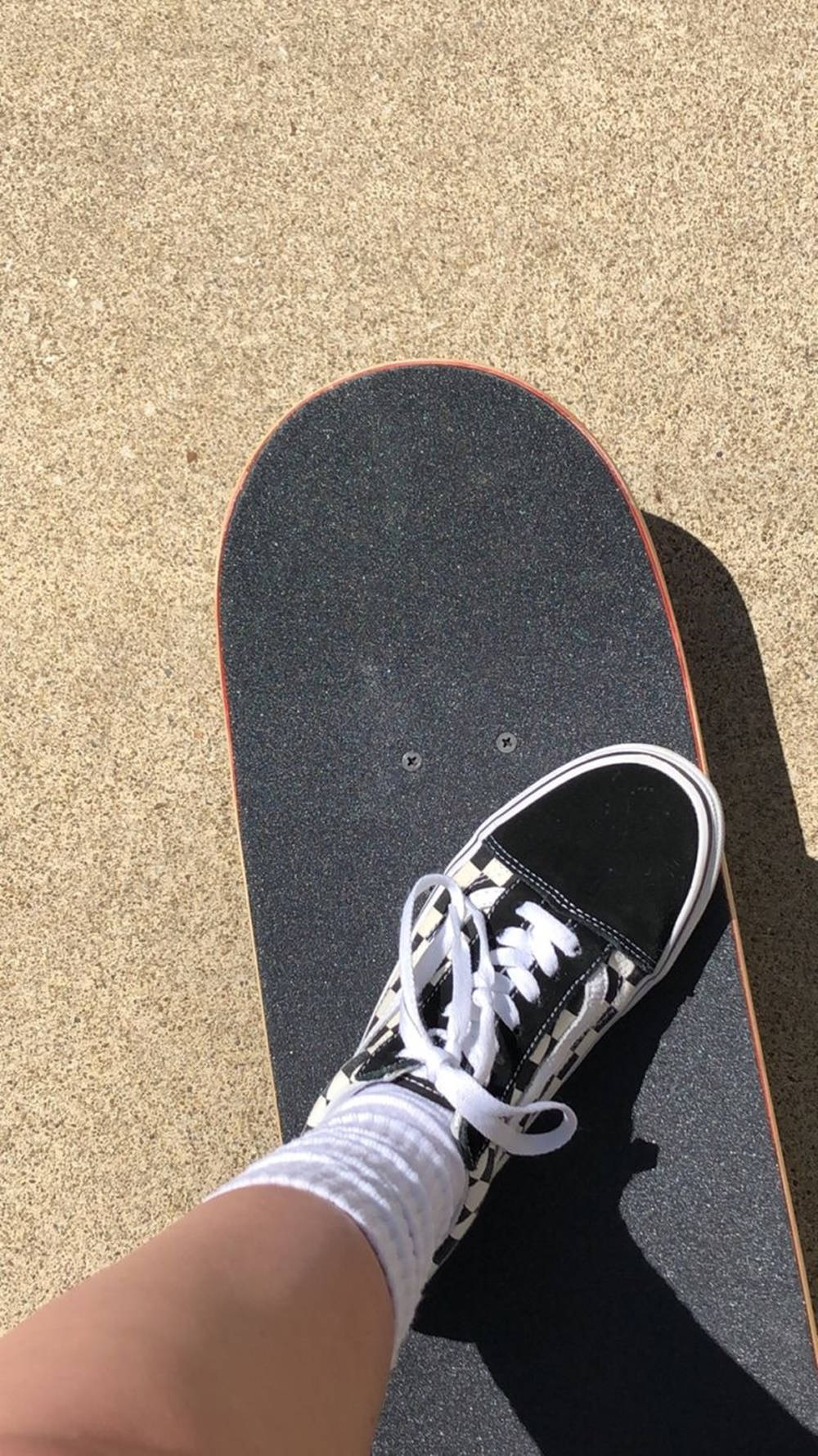 Vans Sk8-Hi鞋與黑色滑板滑手美學 壁紙 — 一隻穿著黑白波鞋的腳企喺陽光照射嘅水泥地上嘅滑板上。