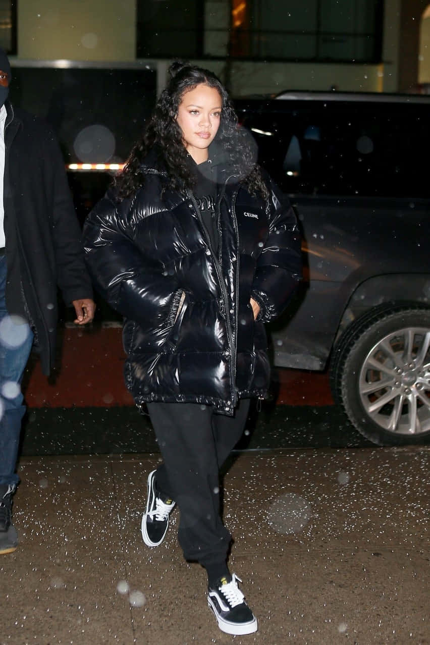 Rihanna 在夜晚雪中行走，身穿黑色羽絨外套和運動鞋。