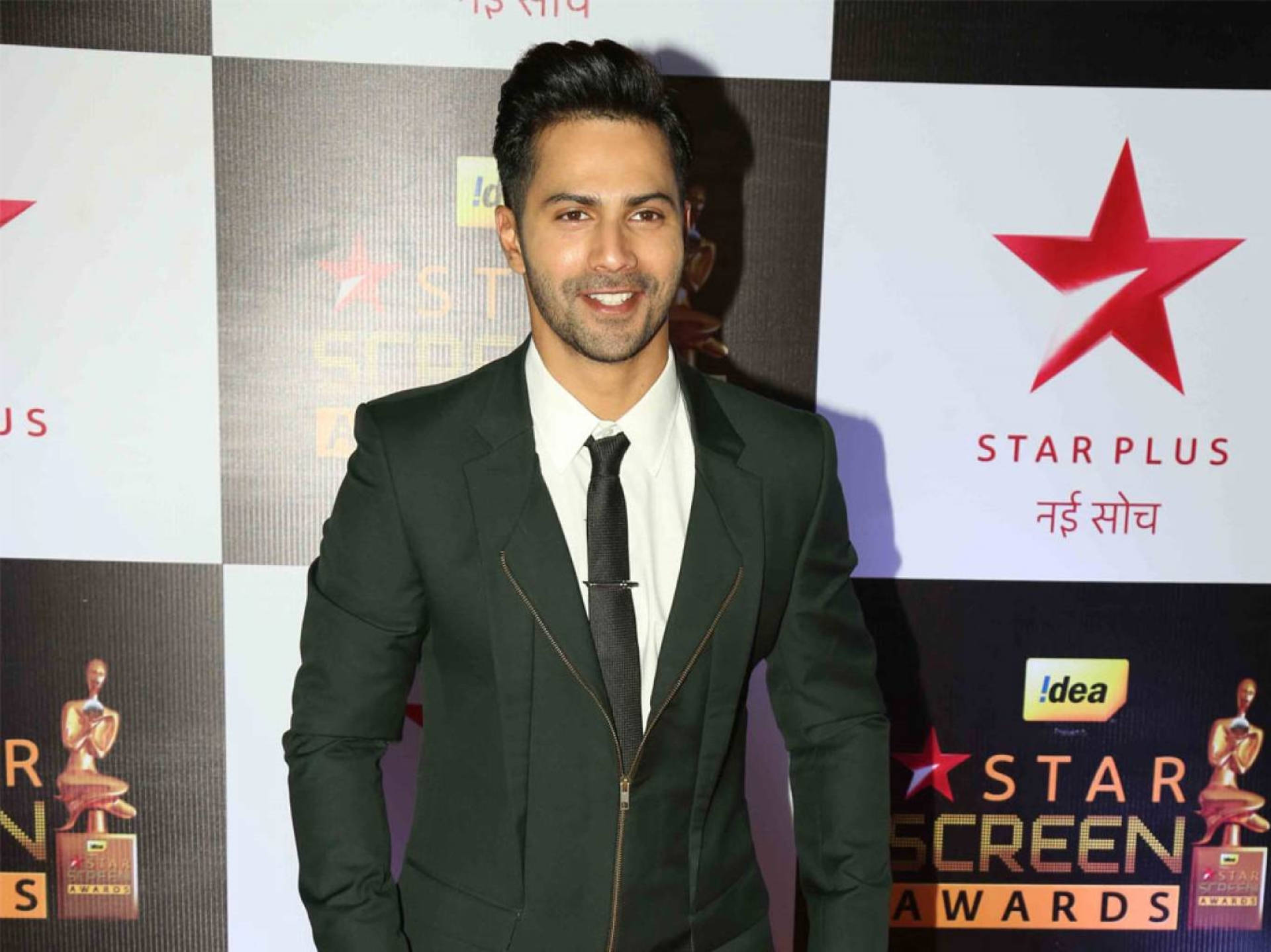 Varun Dhawan出席Star Screen Awards 壁紙 — 一位面帶微笑、身穿深綠色西裝、帶有拉鍊細節的男士，在 Star Screen Awards 紅地毯活動上自信地擺姿勢。