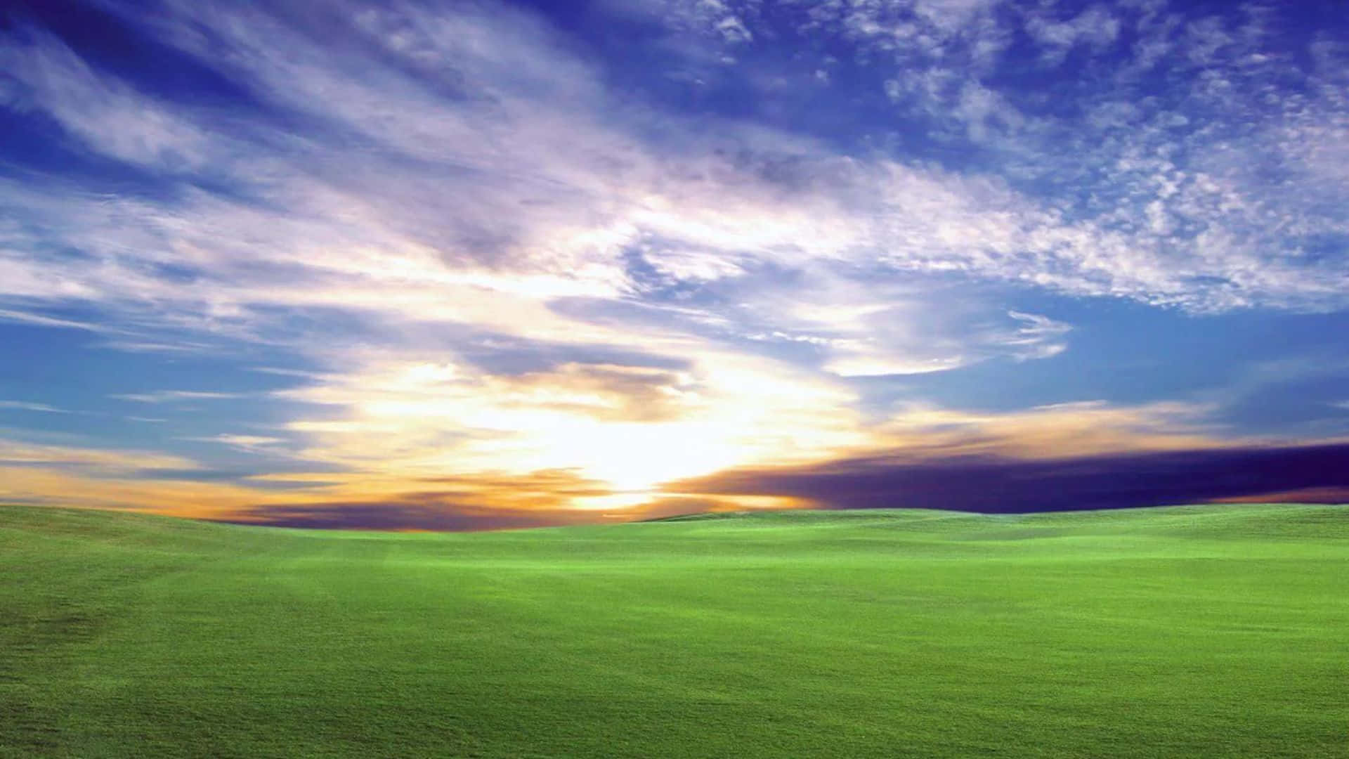  壁紙 — 廣闊的綠色起伏山丘在夕陽色彩和縷縷雲彩繪成的戲劇性天空下延伸。