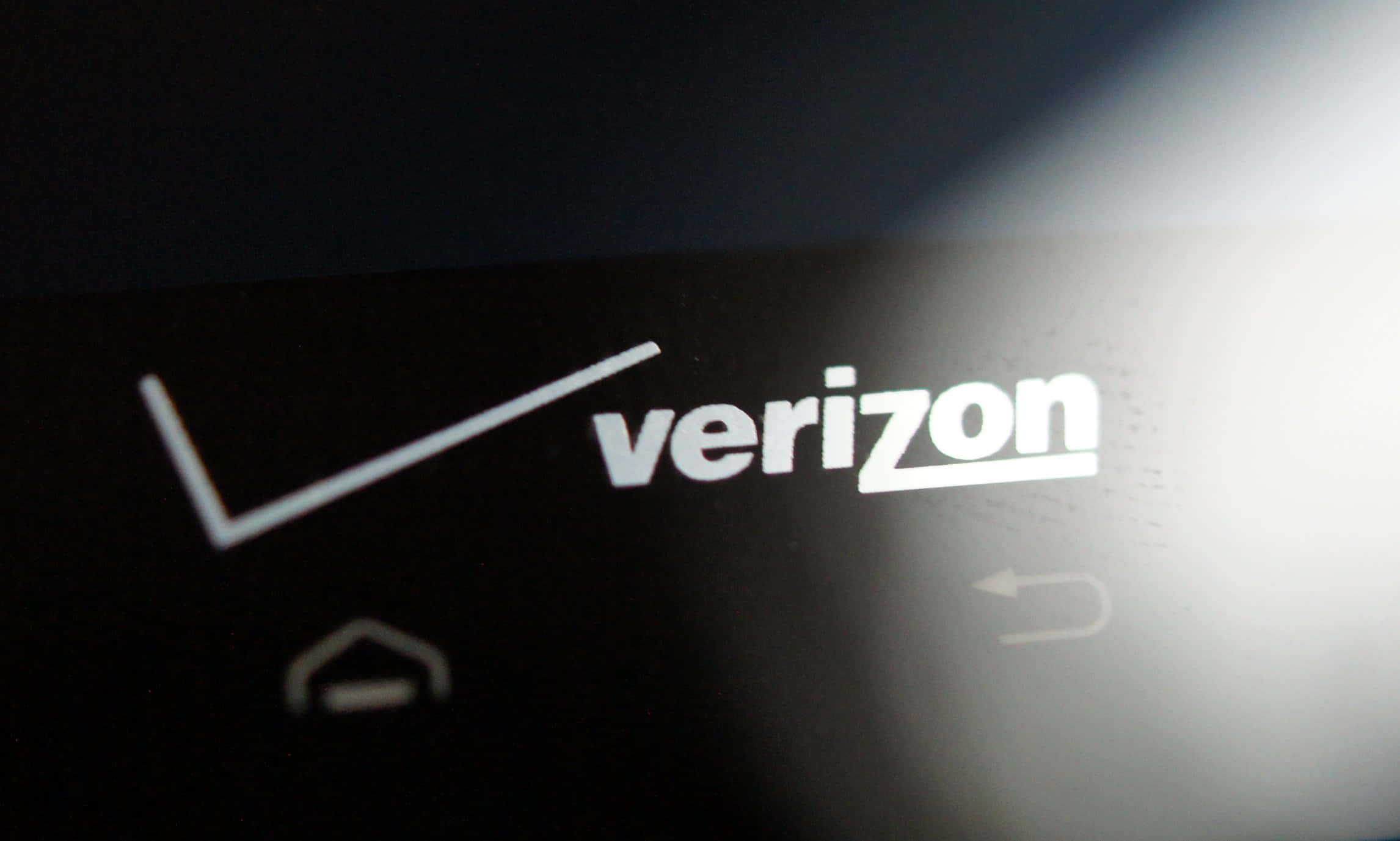 選擇Verizon，體驗無與倫比的無線覆蓋 壁紙 — 特寫Verizon標誌在黑暗屏幕上發出白色光芒，帶有模糊的導航圖標。