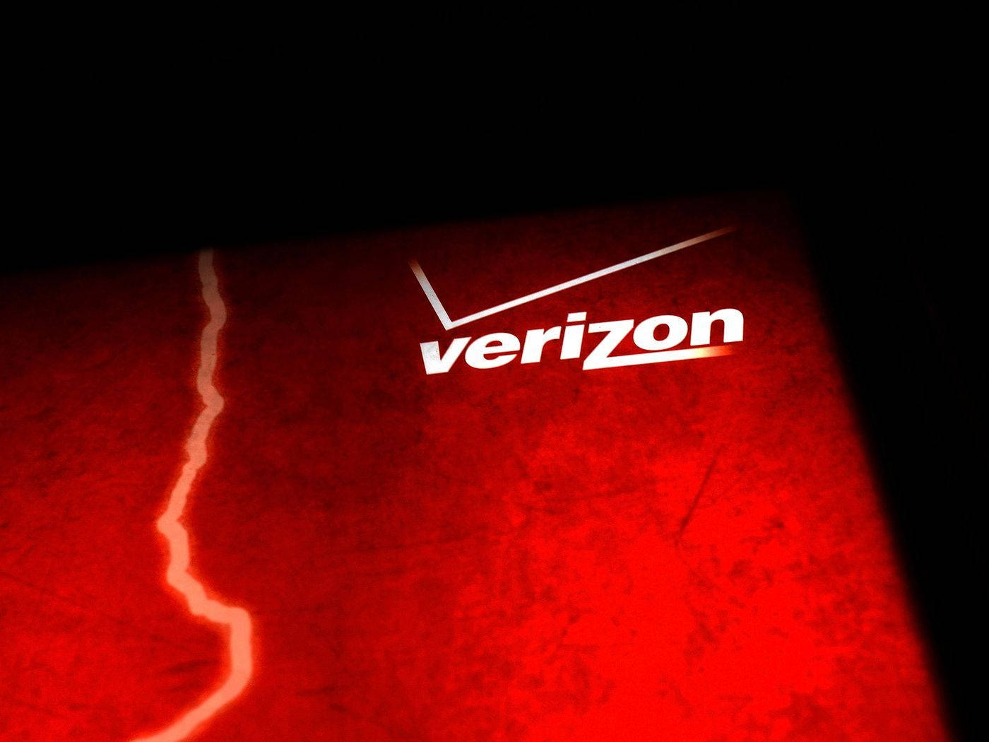 Verizon 鮮紅設計 壁紙 — 一個發光的白色Verizon標誌，位於帶有紋理的紅色表面上，背景黑暗且有一條對角線裂縫。