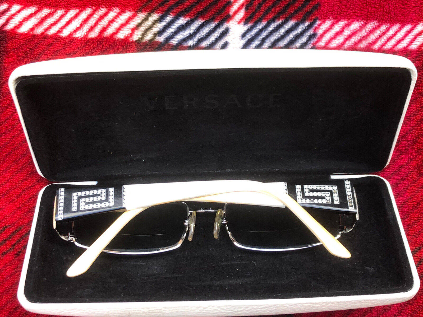 Versace VE1163M 1252女士眼鏡 壁紙 — 奢華Versace太陽眼鏡，象牙白與黑色希臘鑰匙圖案鏡臂，安放在紅色格紋布料上的白色眼鏡盒內。