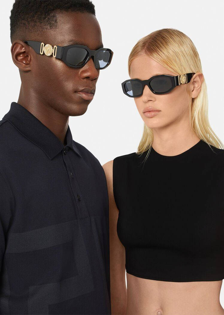Versace 太陽眼鏡模特兒 壁紙 — 一名男子和一名女子在純白色背景前佩戴帶有金色標誌的醒目黑色太陽眼鏡。