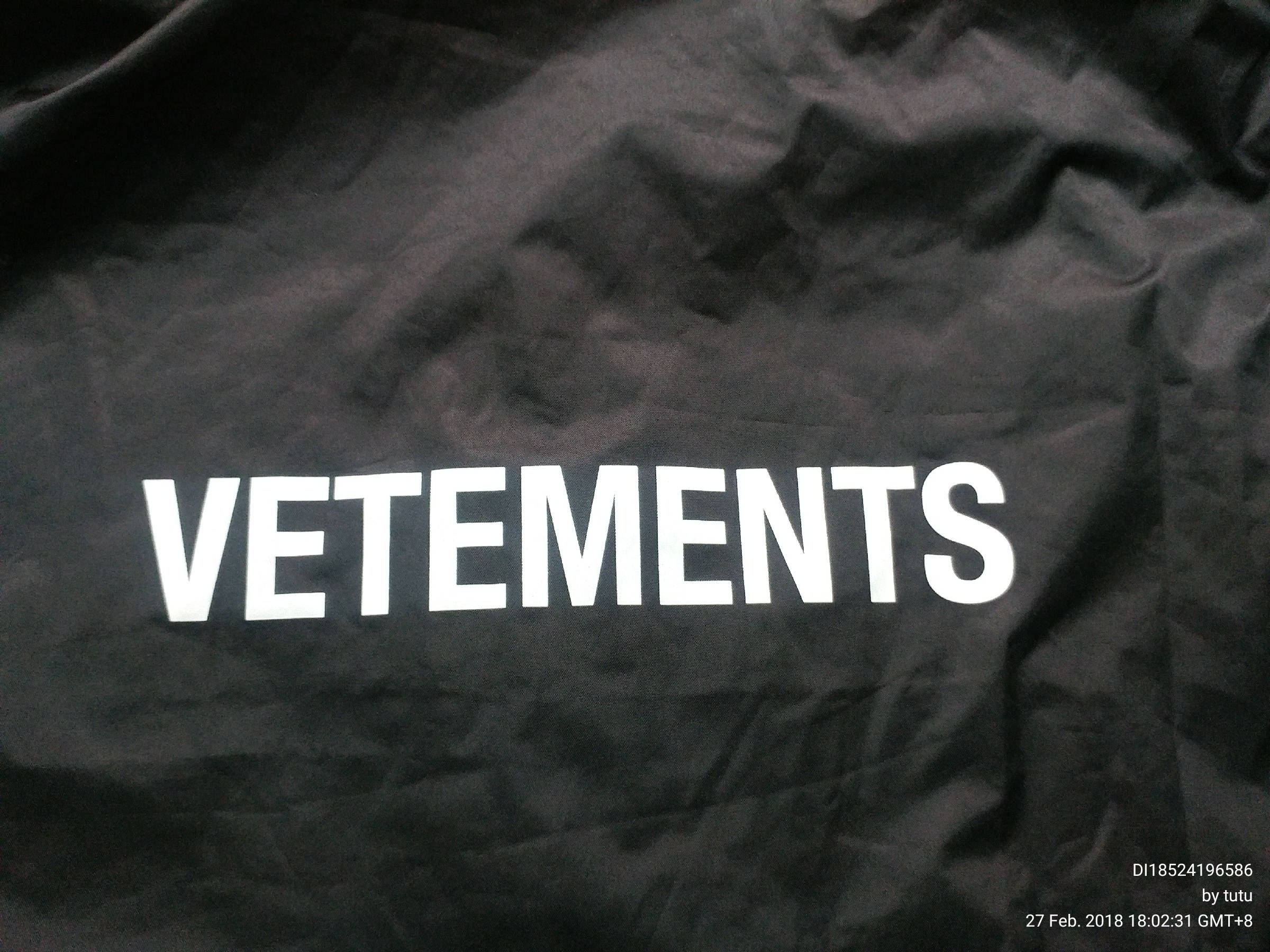 Vetements 黑底白字印花 壁紙 — 特寫：皺褶黑色布料上粗體白色VETEMENTS文字，帶有細微紋理和光線對比。