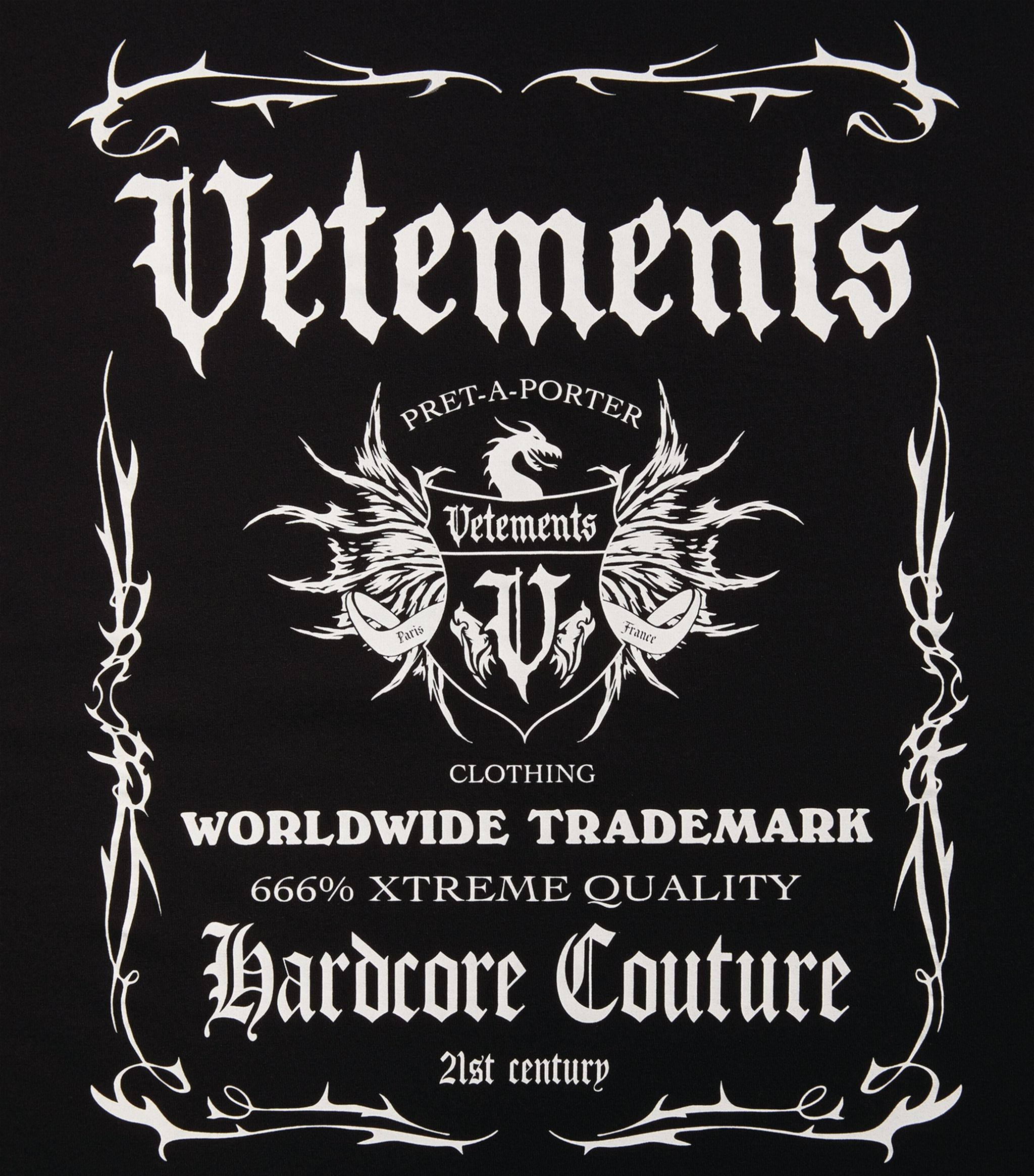 Vetements 黑標誌 壁紙 — 黑色背景，帶有華麗的白色哥德式字體和帶有龍和翅膀的紋章，用於Vetements服裝品牌。