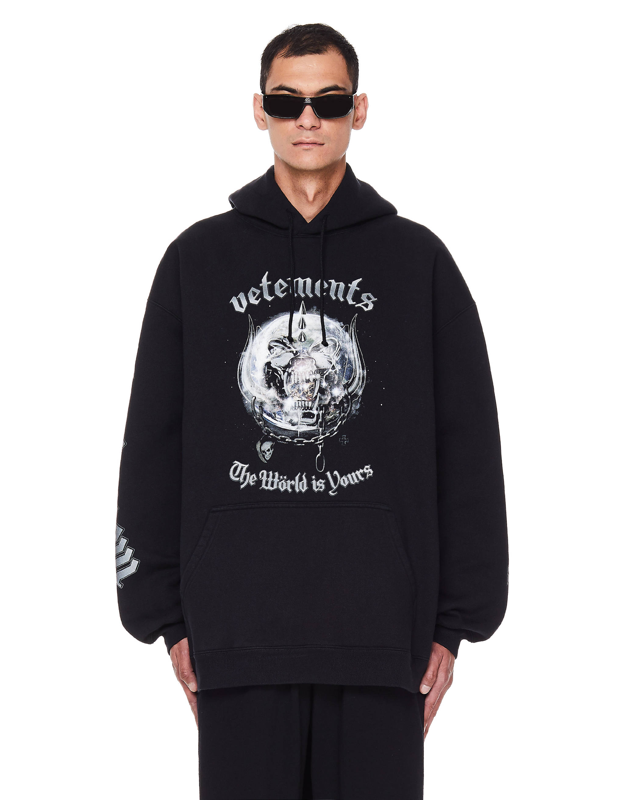 Vetements 「世界屬於你」 壁紙 — 一名戴黑色太陽眼鏡的男子，身穿印有骷髏圖案和文字「Vetements The World is Yours」的 oversized 黑色連帽衫，背景為白色。