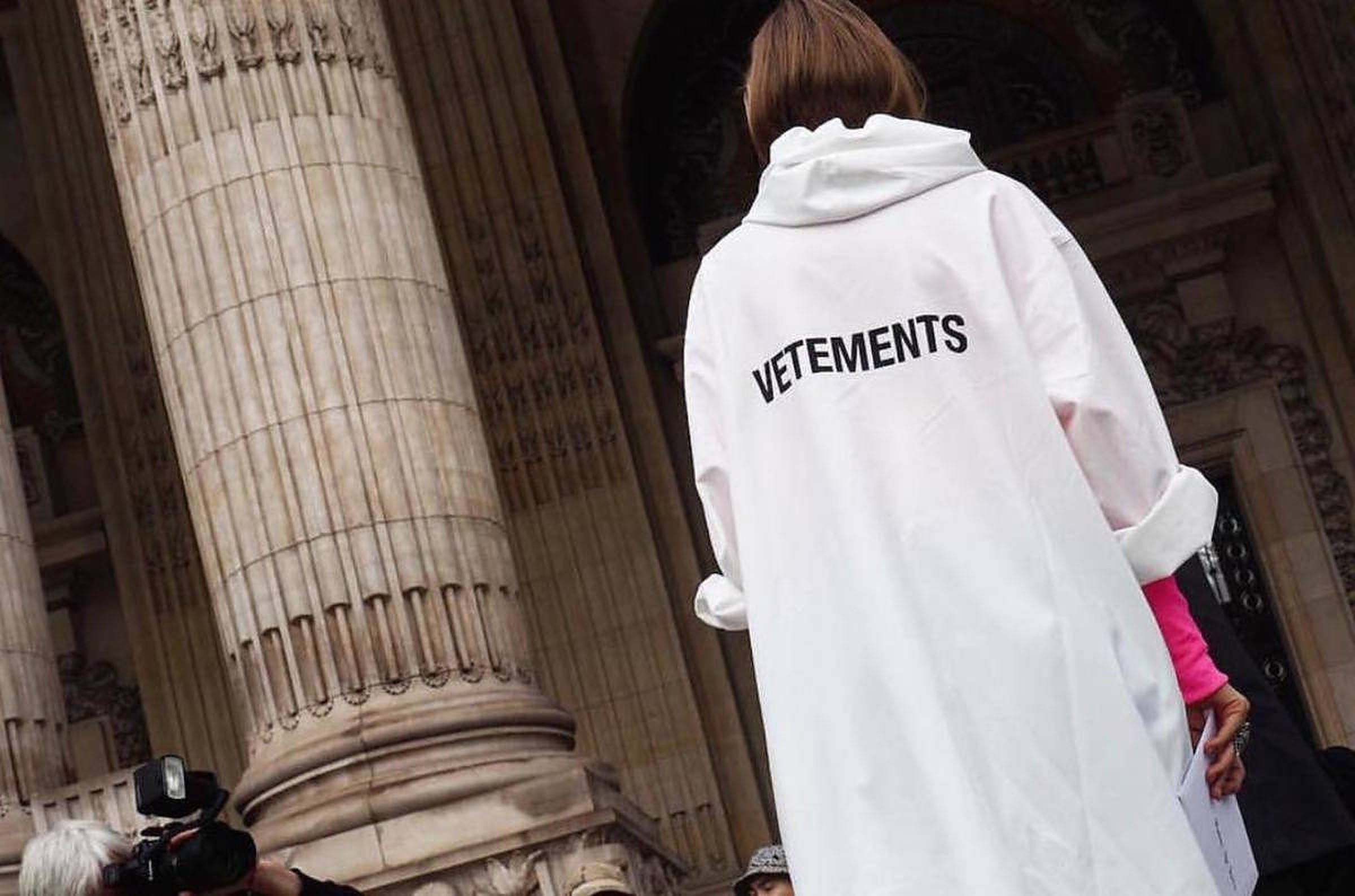 Vetements 白色雨衣 壁紙 — 一個人穿著白色Vetements連帽衫，站在古典建築的巨大石柱前。