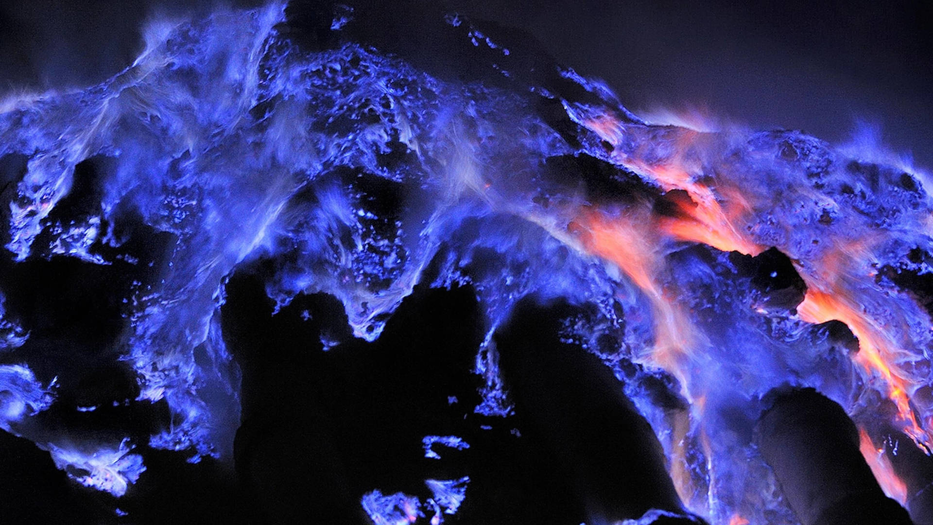 夜間在黑暗的火山岩上噴發的發光藍色和橙色熔岩流。