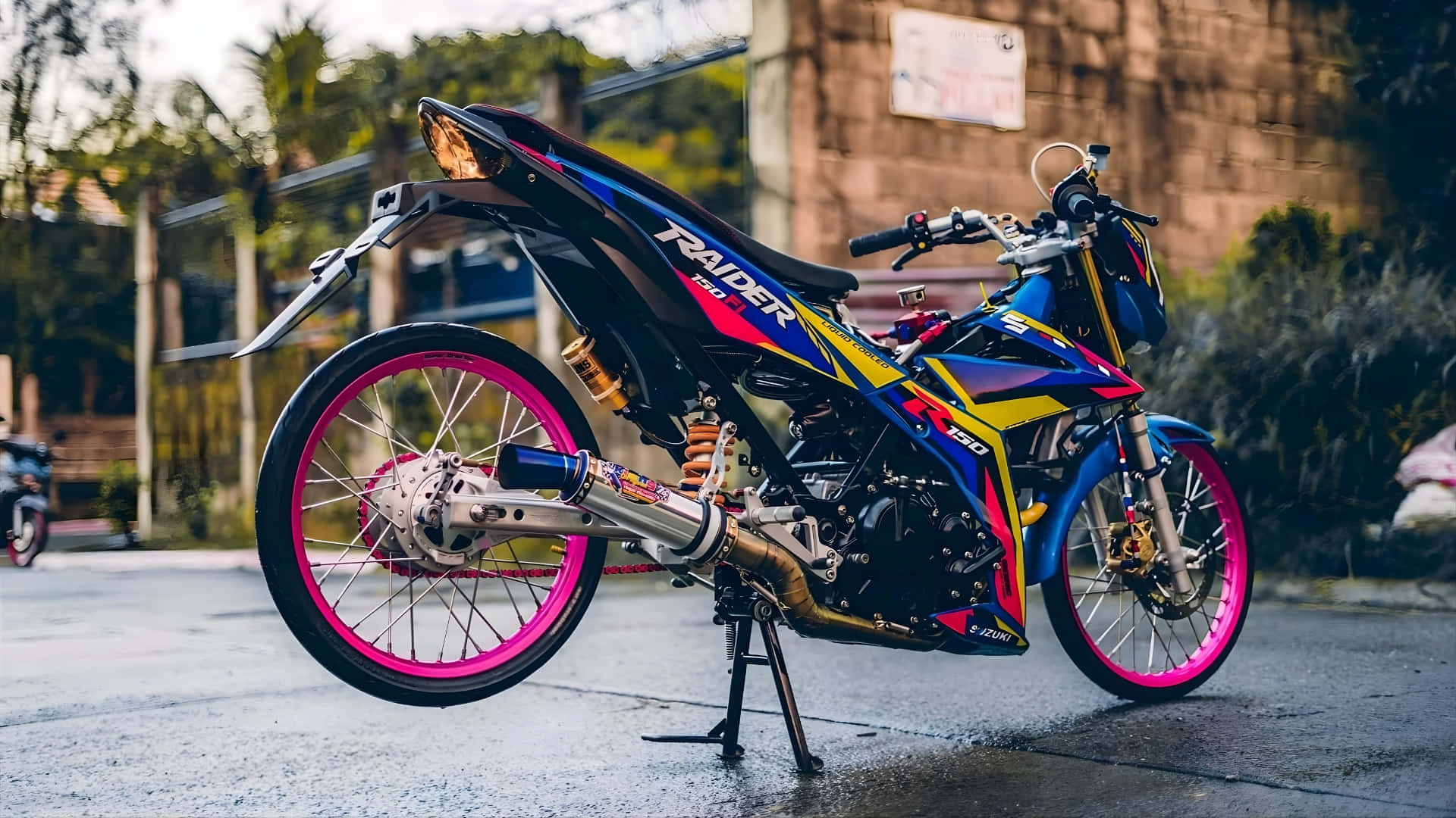  壁紙 — 一架鮮豔藍色和粉紅色的訂製電單車帶有 'RAIDER' 品牌標誌，在柔和日光下停在濕漉漉的路面上。