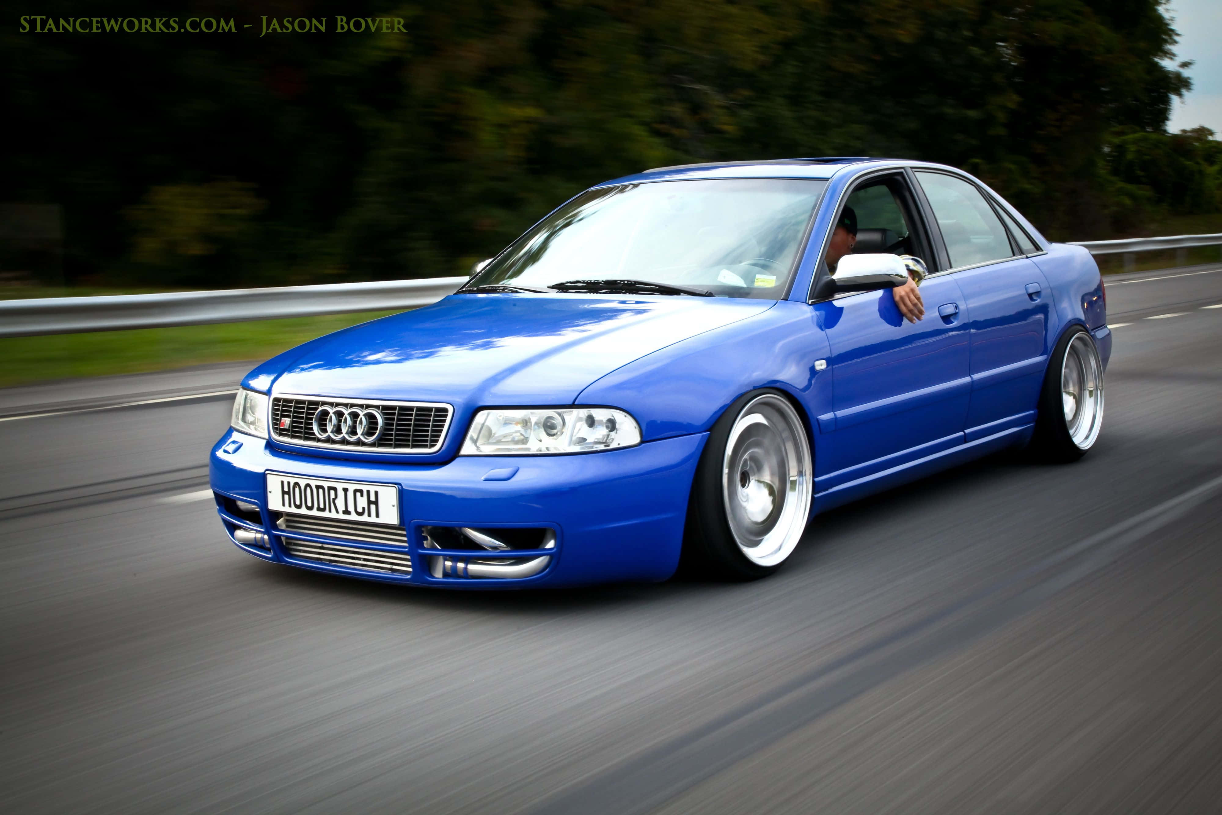 Audi S4 桌布 壁紙 — 一輛充滿活力的藍色奧迪房車，降低懸掛，在模糊的高速公路上飛馳，背景有樹木。